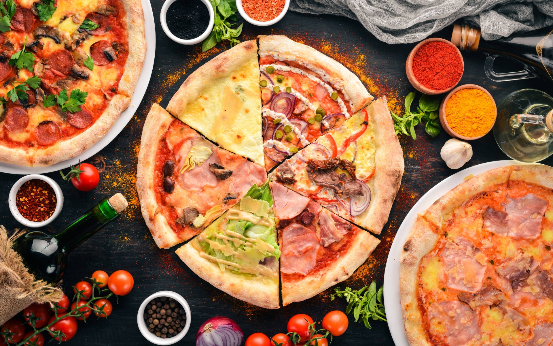 Pizza 桌布 壁紙 — 三款美食披薩配以多種配料，擺放在深色鄉村風格的桌子上，周圍環繞著新鮮食材和香料。