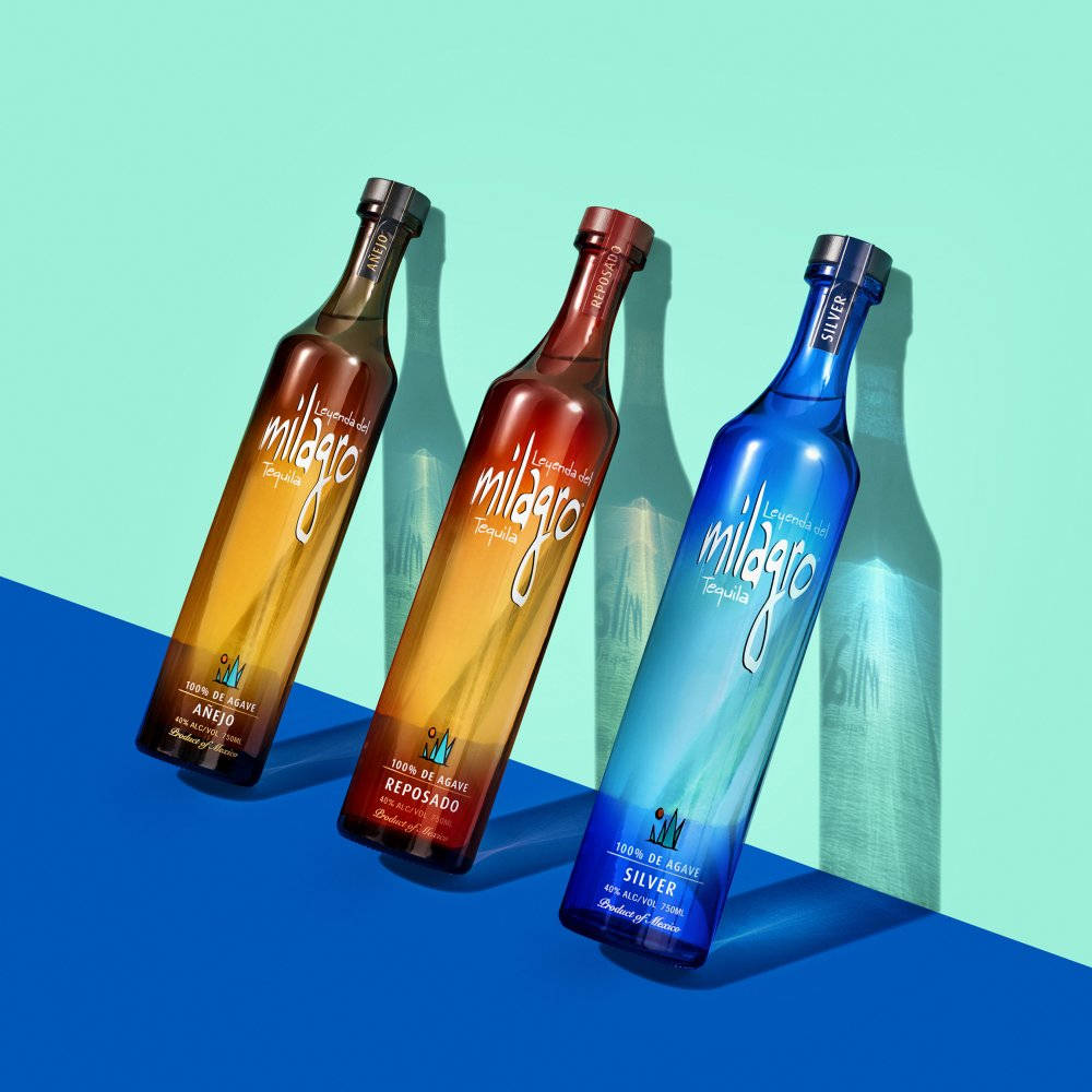 alcohol 桌布 壁紙 — 三款色彩繽紛的Milagro龍舌蘭酒瓶，琥珀色、紅色和藍色，以對角線排列在分為藍綠色和藍色的背景上，帶有銳利的陰影。