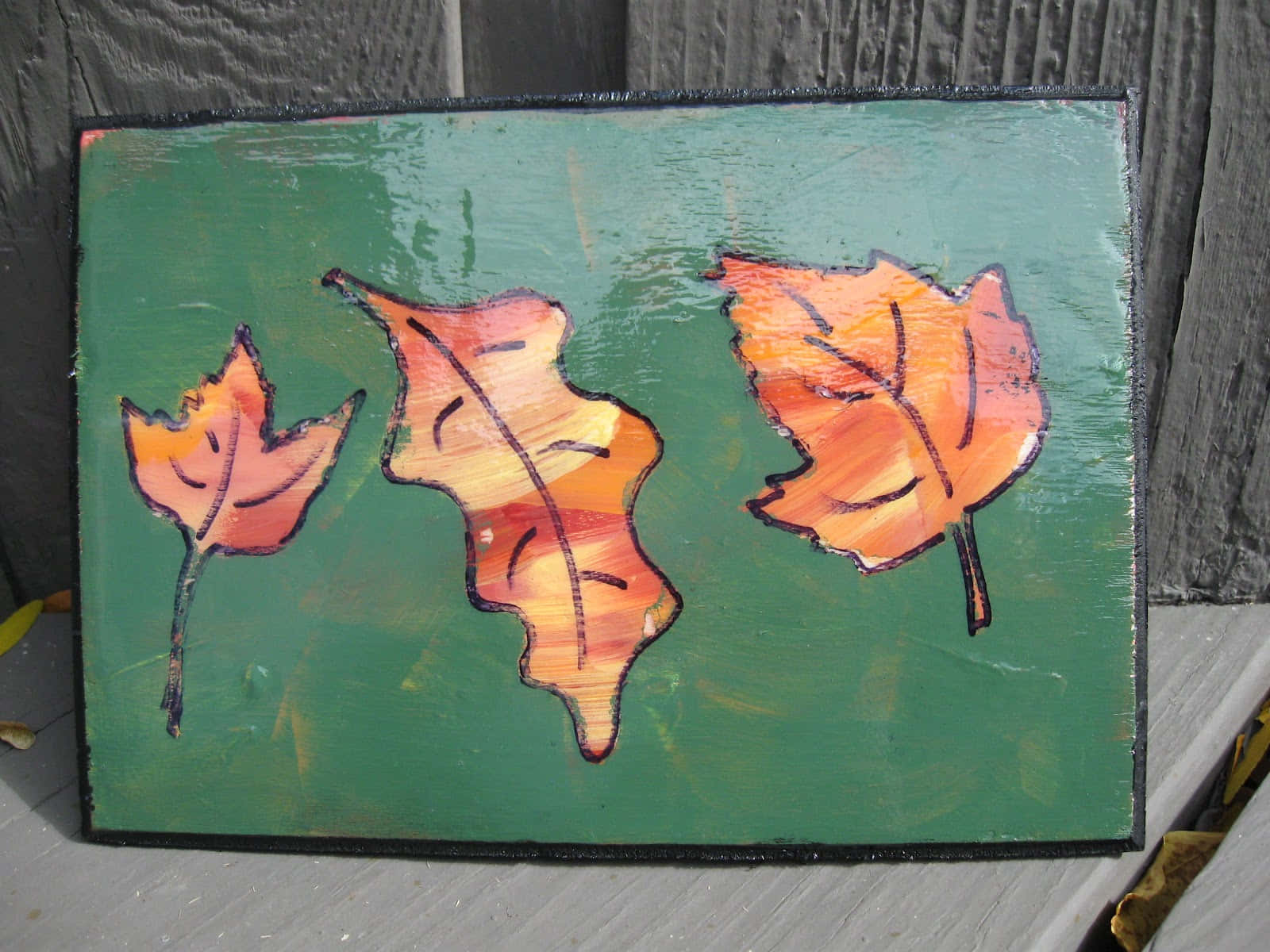 Fall Crafts 桌布 壁紙 — 三片塗成橙色和黃色的秋葉，放在綠色紋理畫布上，背景是風化的木柵欄。