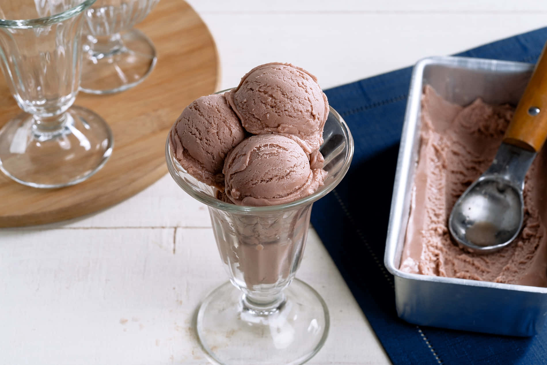 Ice Cream 桌布 壁紙 — 三球濃郁巧克力冰淇淋放在玻璃聖代杯內，旁邊有一個金屬桶和木柄冰淇淋勺。