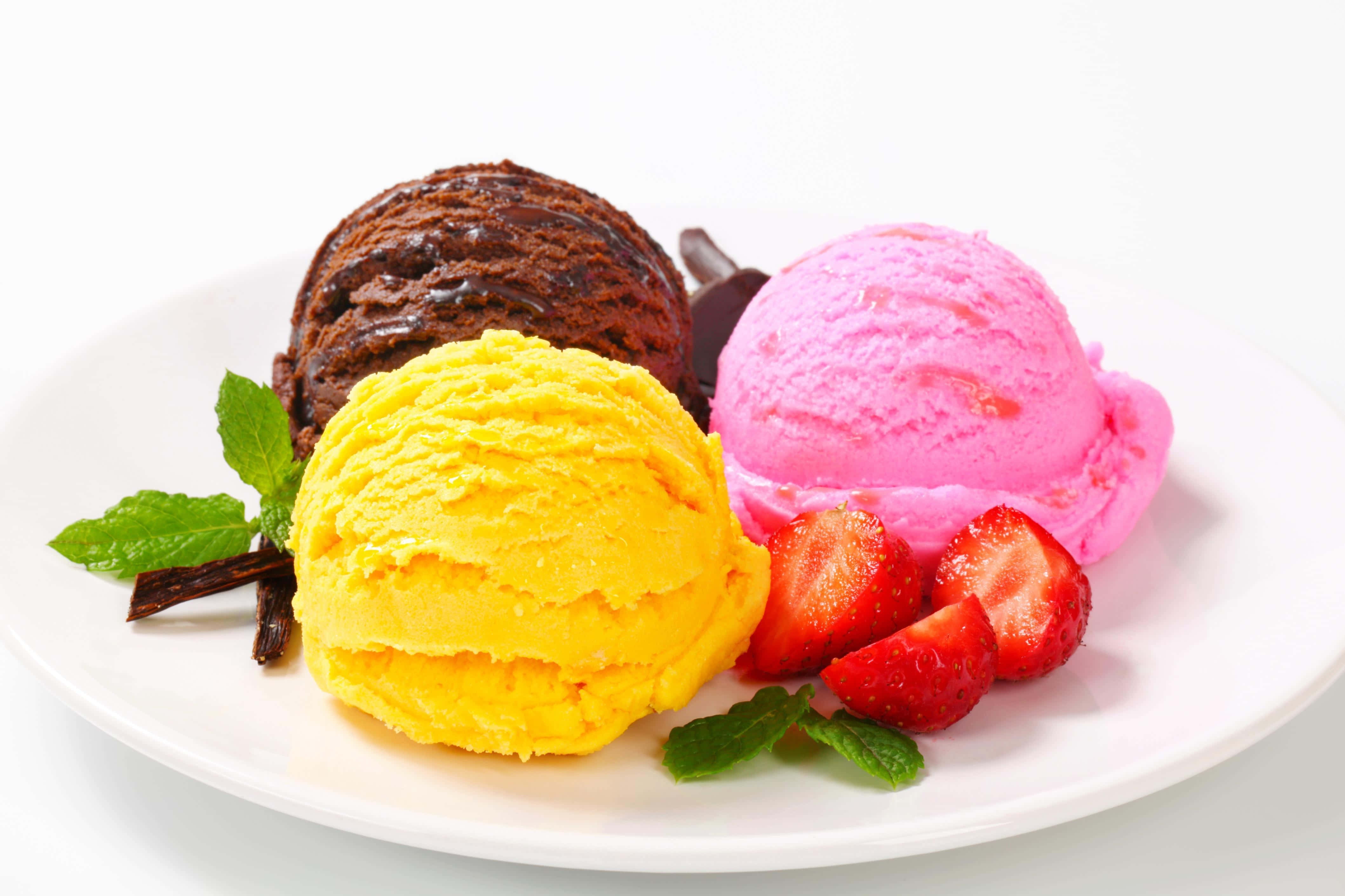 Ice Cream 桌布 壁紙 — 三球色彩鮮豔的巧克力、黃色和草莓冰淇淋，配上新鮮薄荷葉和切片草莓，放在白色盤子上。