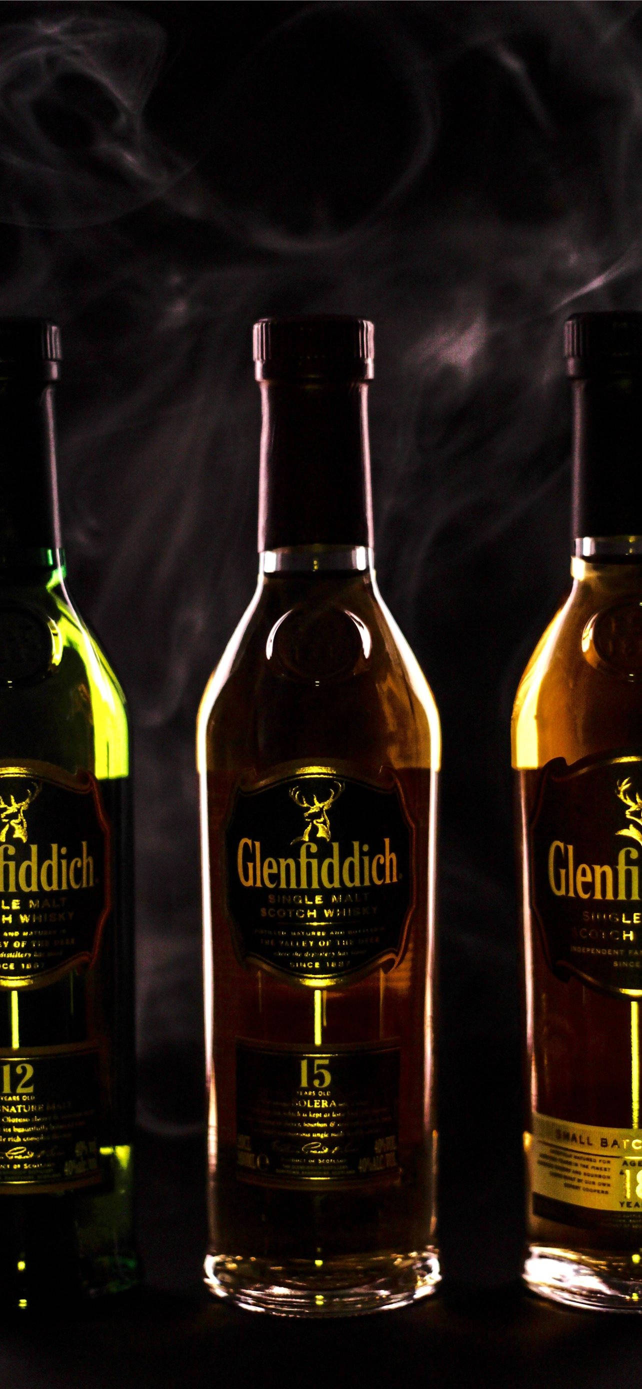 drinks 桌布 壁紙 — 三瓶 Glenfiddich 威士忌在煙霧瀰漫的黑暗背景下，以戲劇性的燈光溫暖地發光。