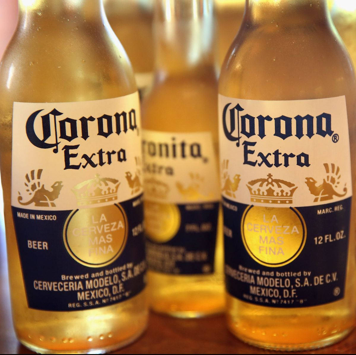 corona 桌布 壁紙 — 三瓶Corona Extra啤酒，裝有金色液體和標誌性標籤，緊密地放在木質表面上。