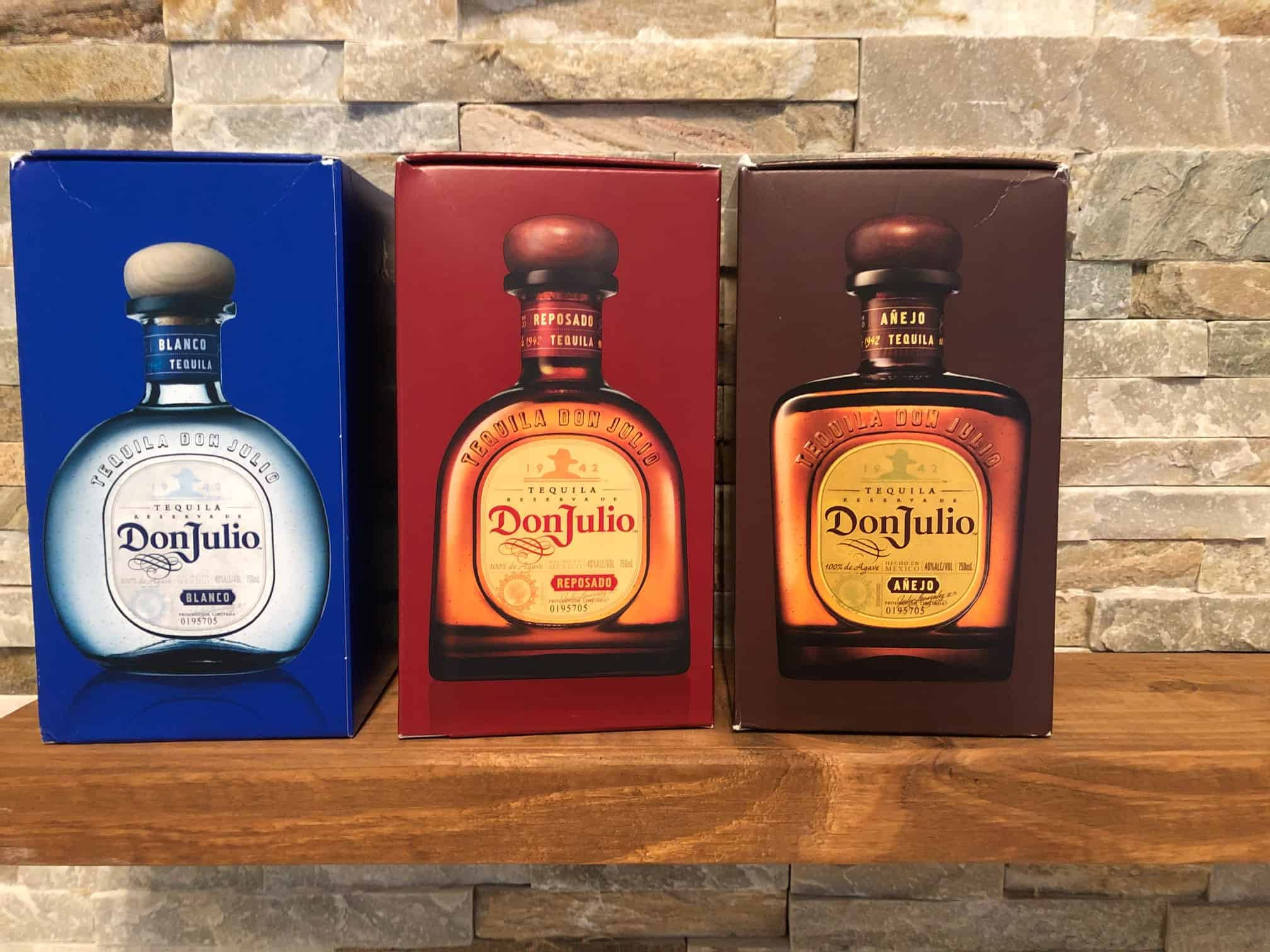 Box 桌布 壁紙 — 三瓶Don Julio龍舌蘭酒連同其彩色盒子整齊地放在石牆前的木架上。