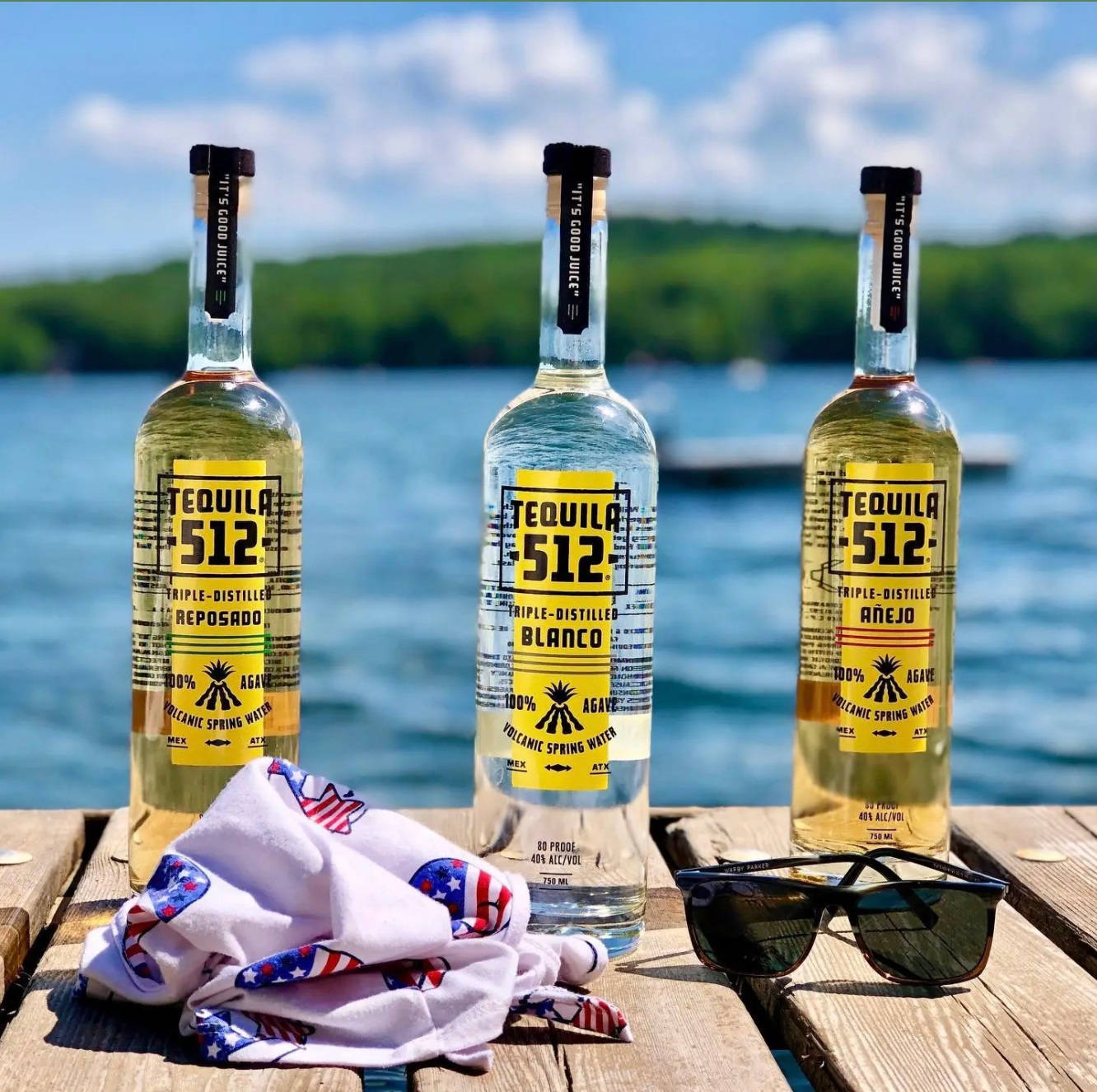 drinks 桌布 壁紙 — 三瓶Tequila 512放在木碼頭上，旁邊有太陽眼鏡和美國國旗頭巾，背景是湖泊和森林。