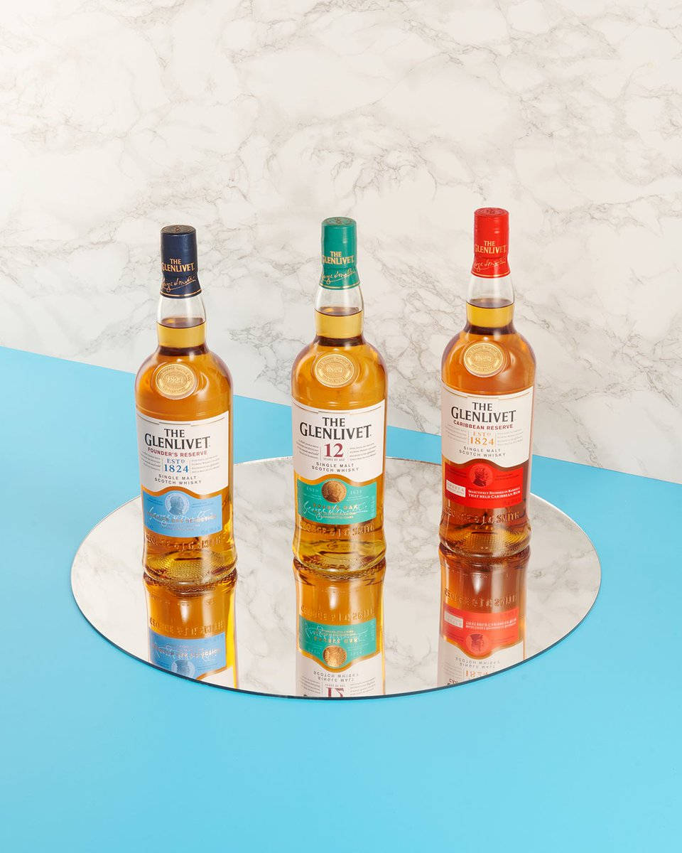  壁紙 — 三瓶帶有不同顏色瓶蓋的The Glenlivet威士忌酒瓶，放置在藍色背景下的反光大理石托盤上。