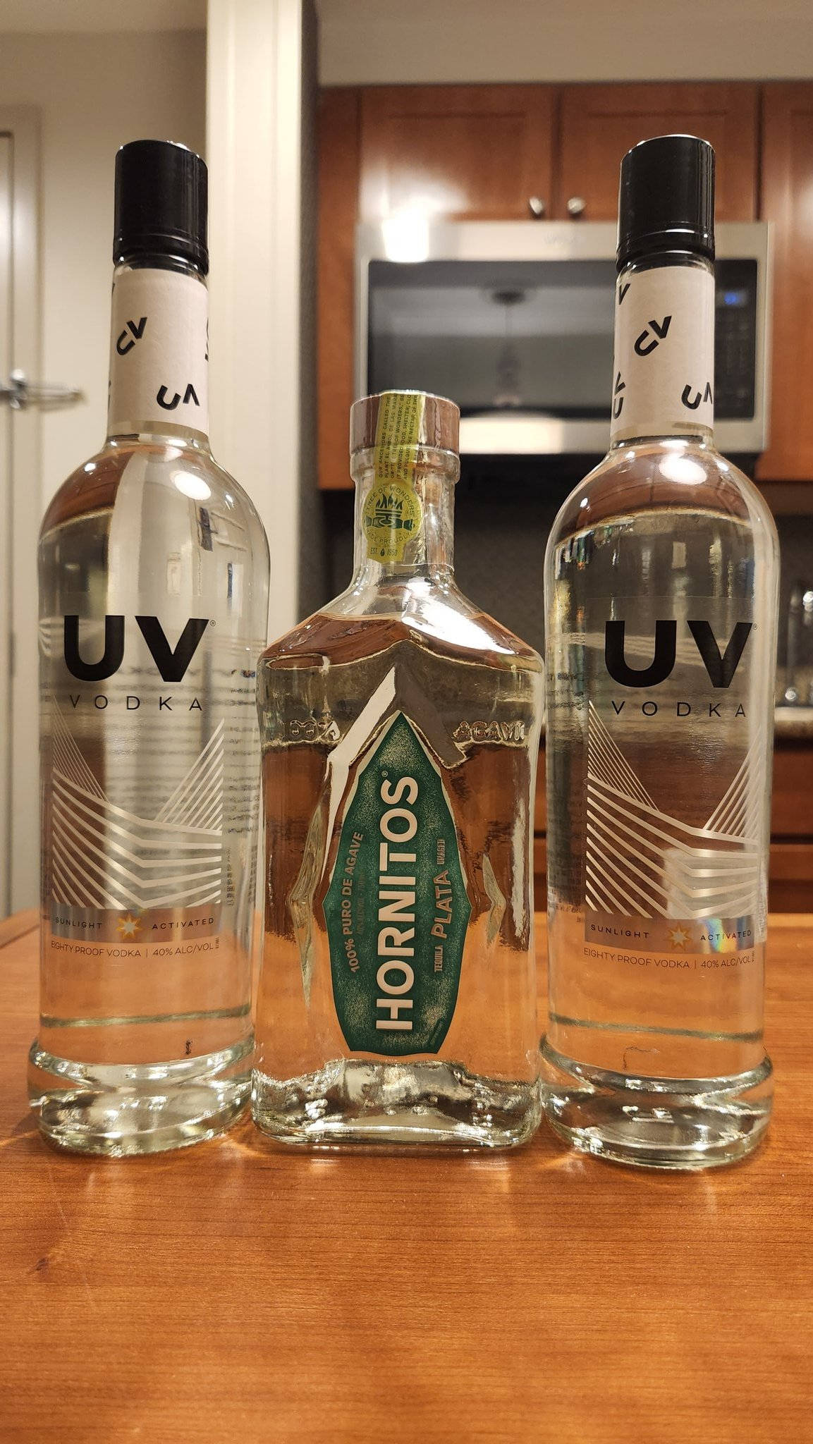 drinks 桌布 壁紙 — 三瓶清澈伏特加酒，包括UV和Hornitos Plata，放在廚房的木製檯面上。
