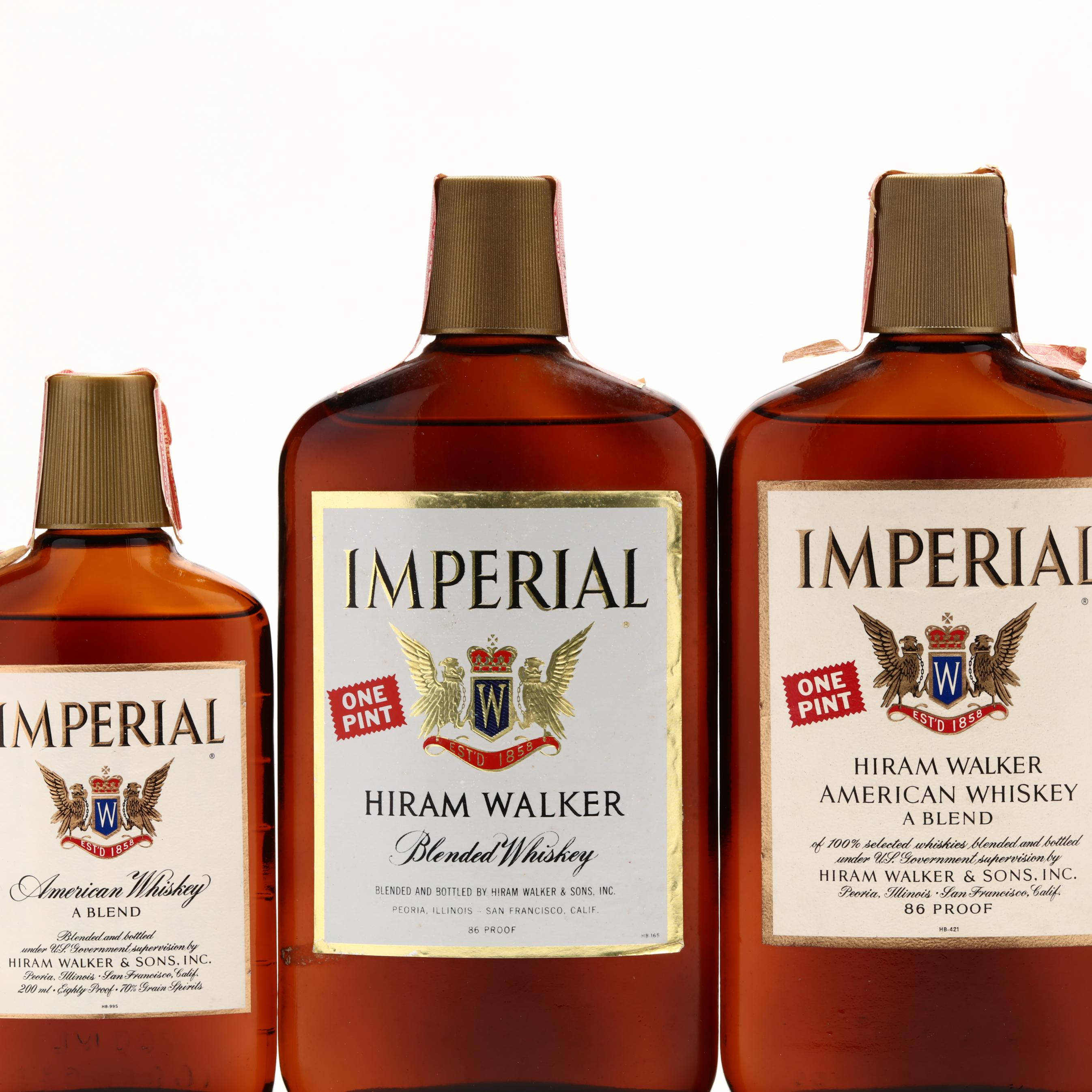 alcohol 桌布 壁紙 — 三瓶琥珀色玻璃瓶裝 Imperial American Whiskey，配有金色瓶蓋和復古標籤，在純白背景前整齊排列。