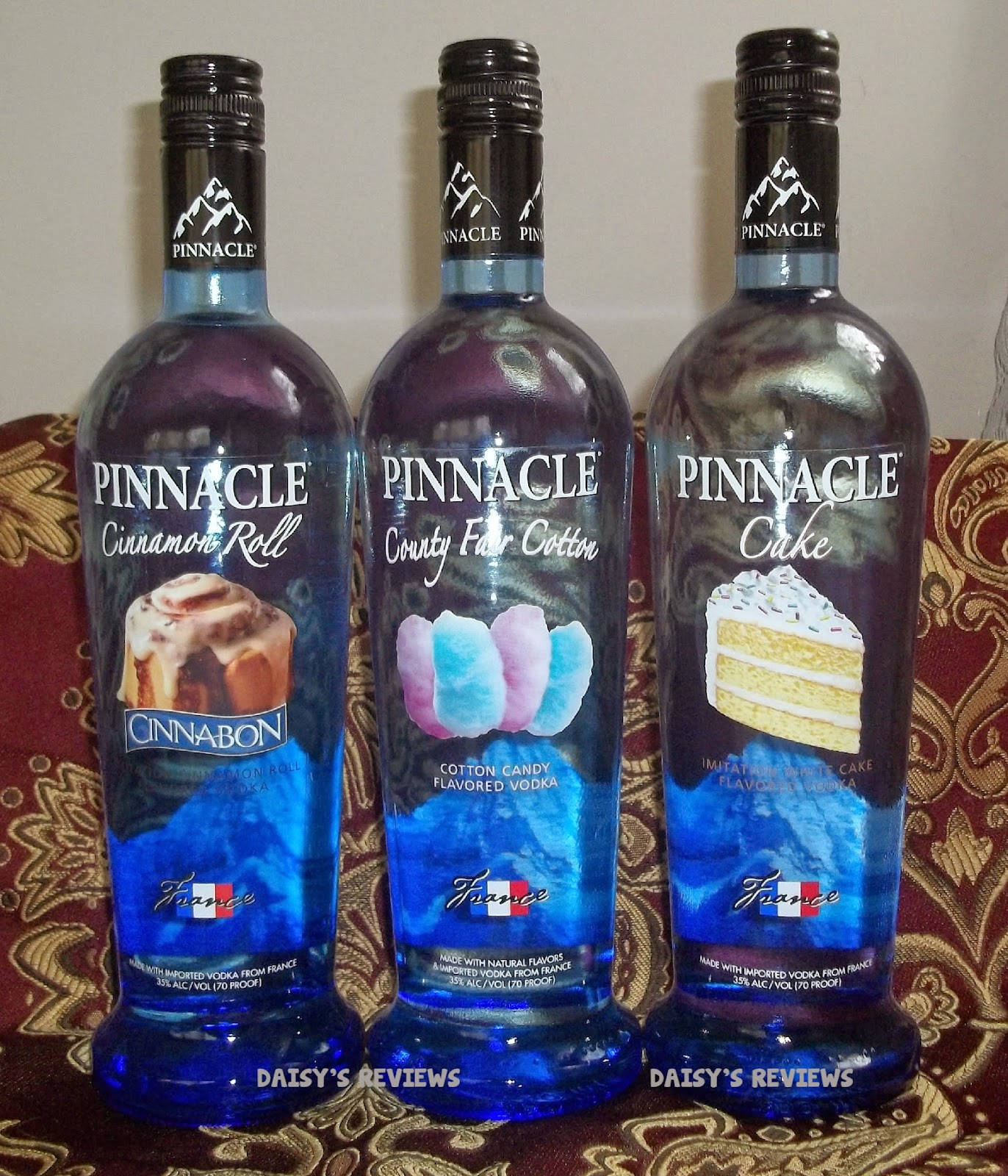 bottle 桌布 壁紙 — 三瓶藍色Pinnacle調味伏特加並排放在紅色和金色圖案布料上。