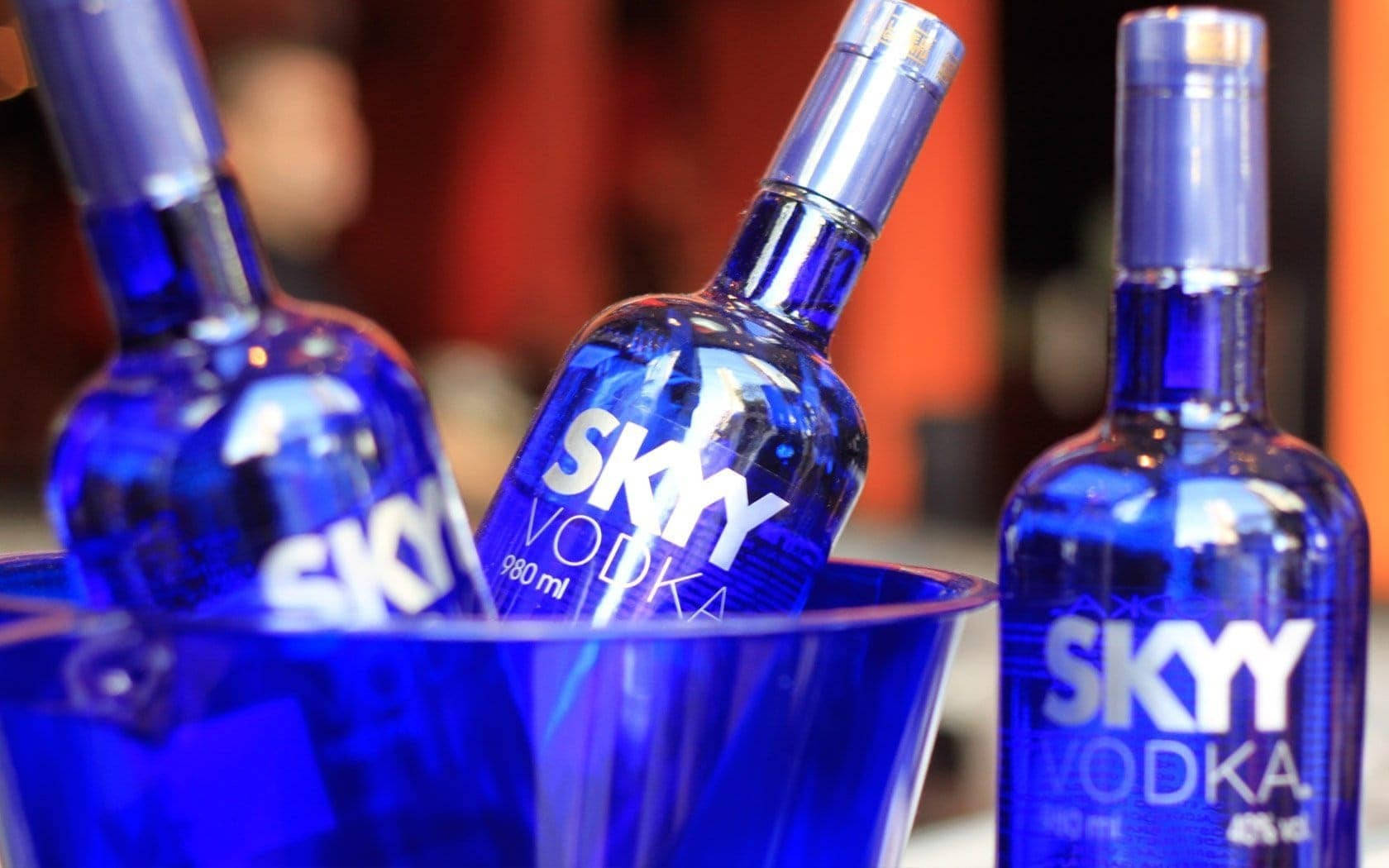 Drink 桌布 壁紙 — 三瓶藍色Skyy伏特加在一個相配的藍色冰桶中冷藏，背景溫暖模糊。
