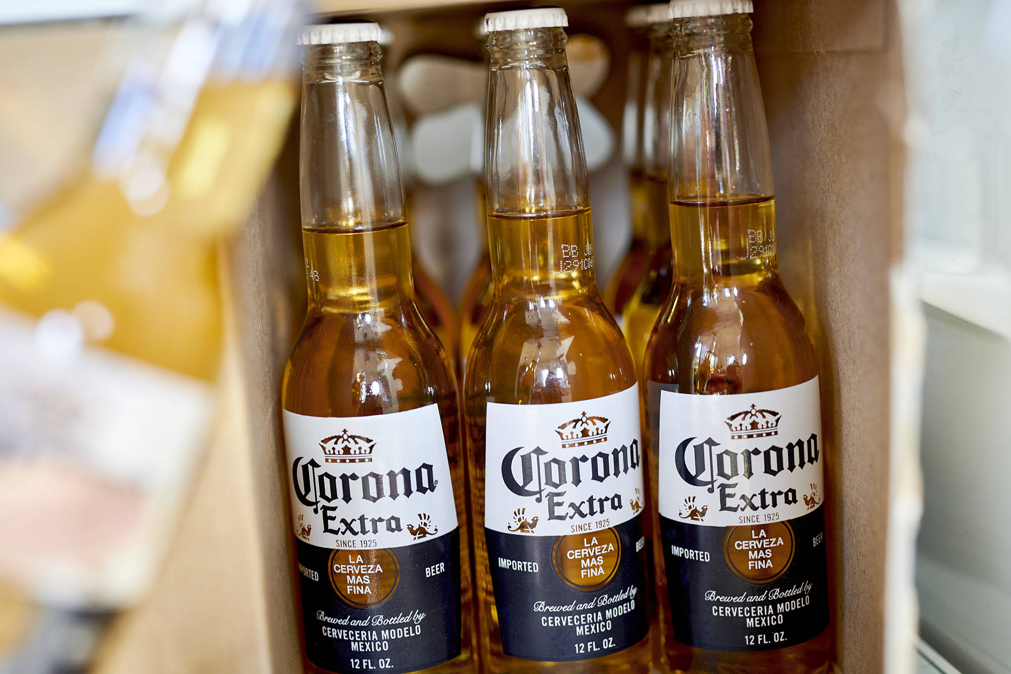 corona 桌布 壁紙 — 三瓶裝有金色液體的Corona Extra啤酒瓶放在一個紙箱中，背景柔和模糊。