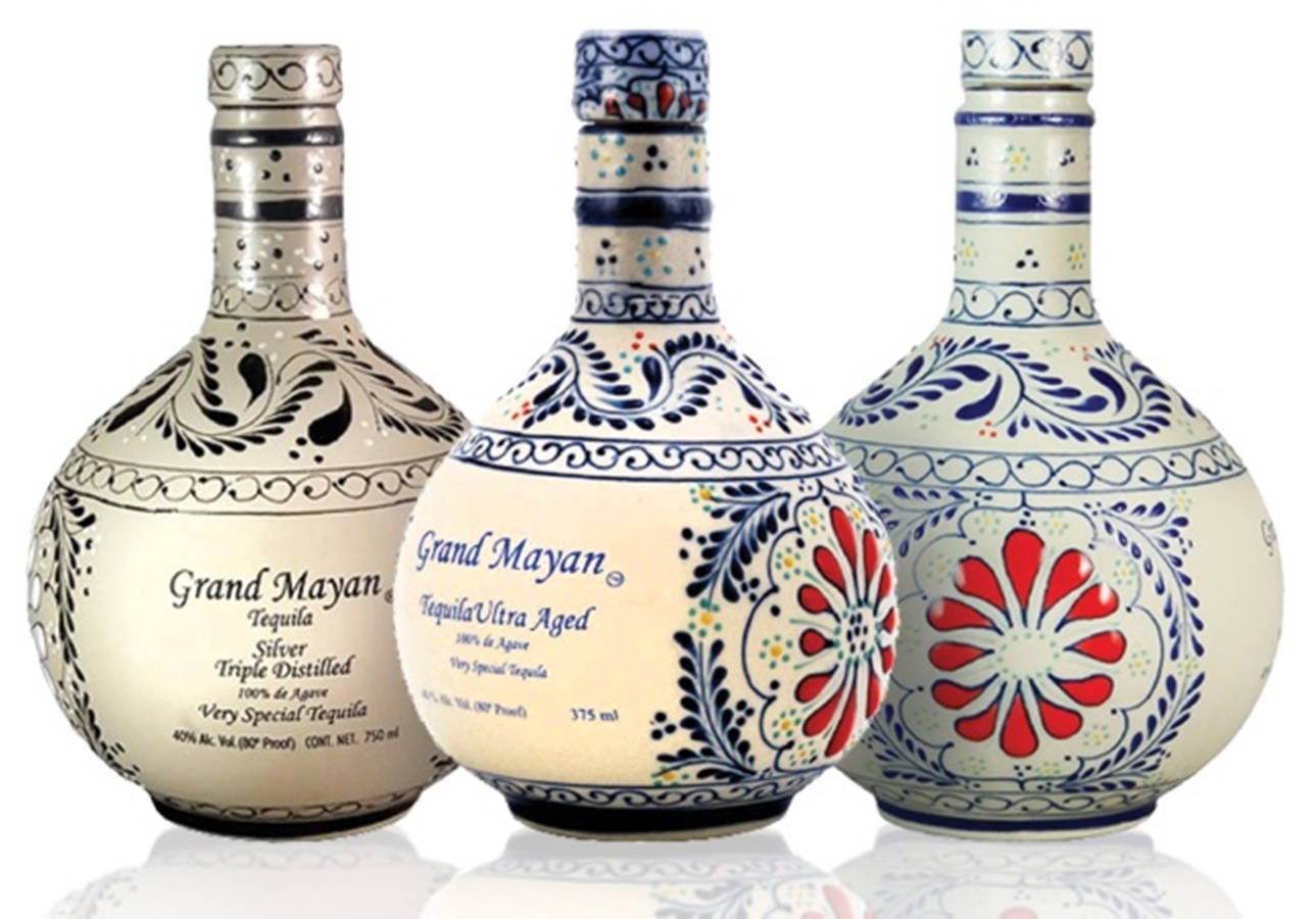 alcohol 桌布 壁紙 — 三瓶裝飾華麗的Grand Mayan龍舌蘭酒瓶，帶有花卉圖案，排列在白色背景前。