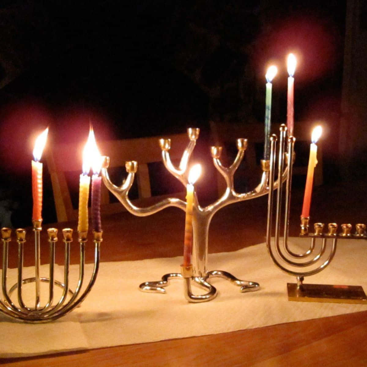 光明節 桌布 壁紙 — 三盞點亮的燭台（Menorah）在黑暗的夜晚背景下，桌上彩色蠟燭溫暖地閃耀。