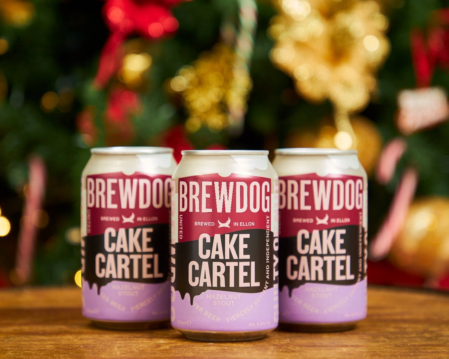 Drink 桌布 壁紙 — 三罐BrewDog Cake Cartel啤酒放在木質表面上，背景是節日氣氛的模糊聖誕樹。