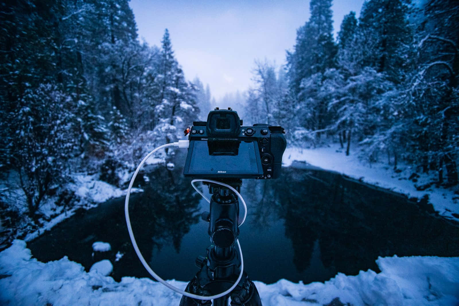 Nature Landscape 桌布 壁紙 — 三腳架上的相機面向一片被雪覆蓋的森林，倒映在黃昏天空下平靜的冬季溪流中。