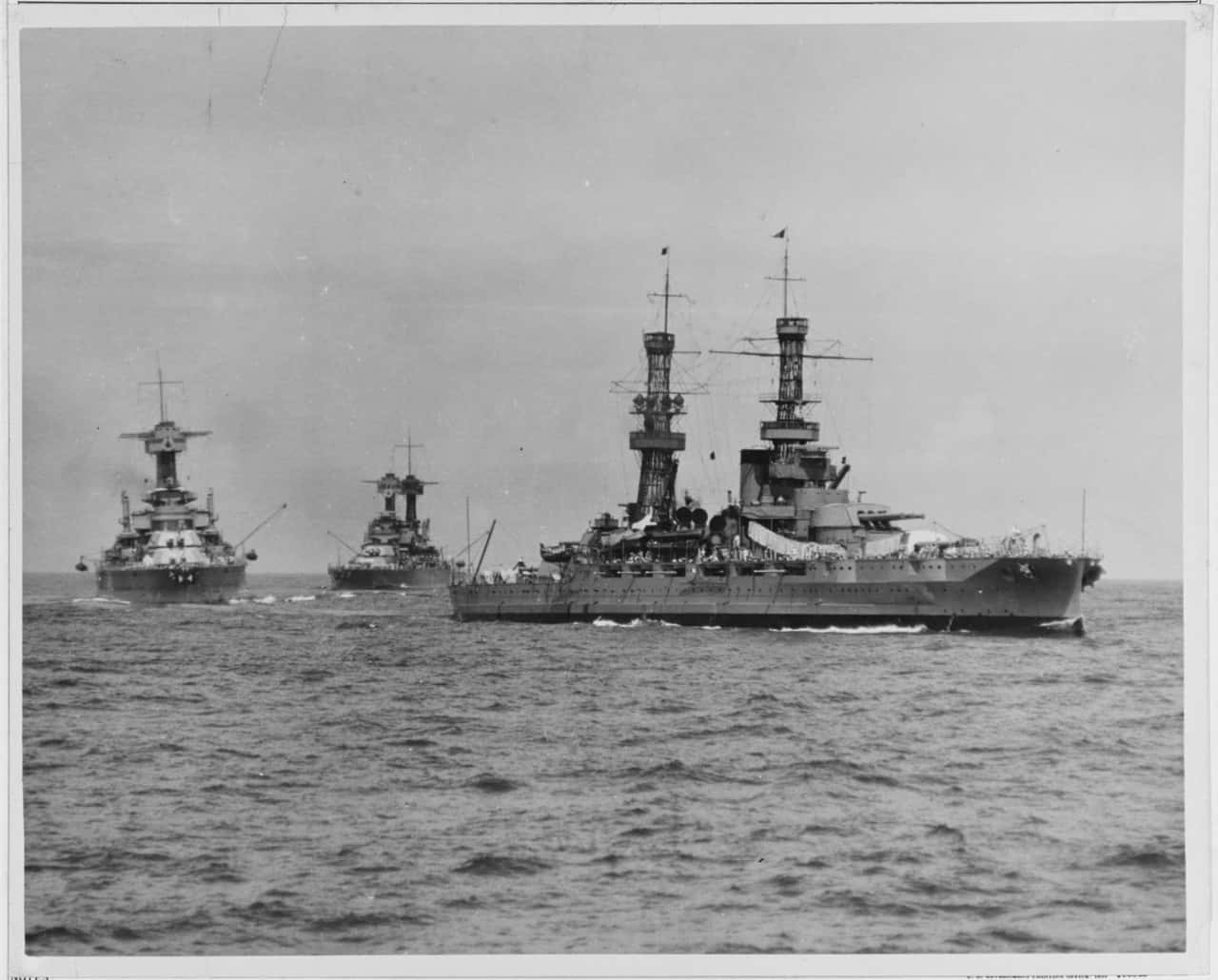 Battleships 桌布 壁紙 — 三艘威嚴的戰艦在陰天之下，於波濤洶湧的海面上編隊航行，這是一張歷史性的黑白照片。
