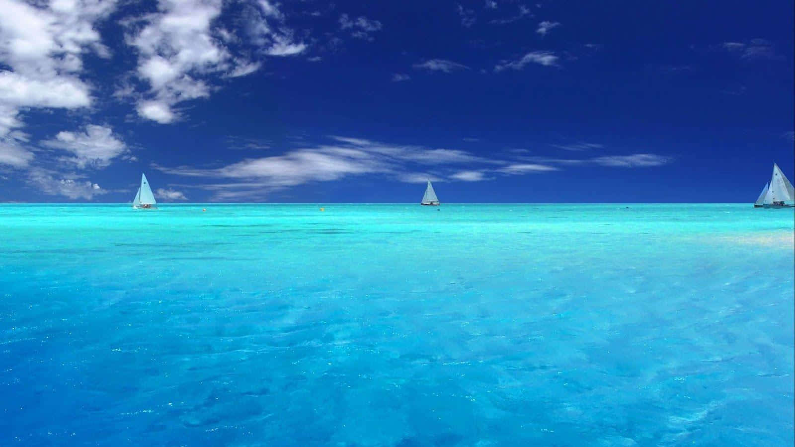 海洋藍 桌布 壁紙 — 三艘帆船在晶瑩剔透的碧綠海水上滑行，頭頂是廣闊的深藍色天空，點綴著蓬鬆的白雲。