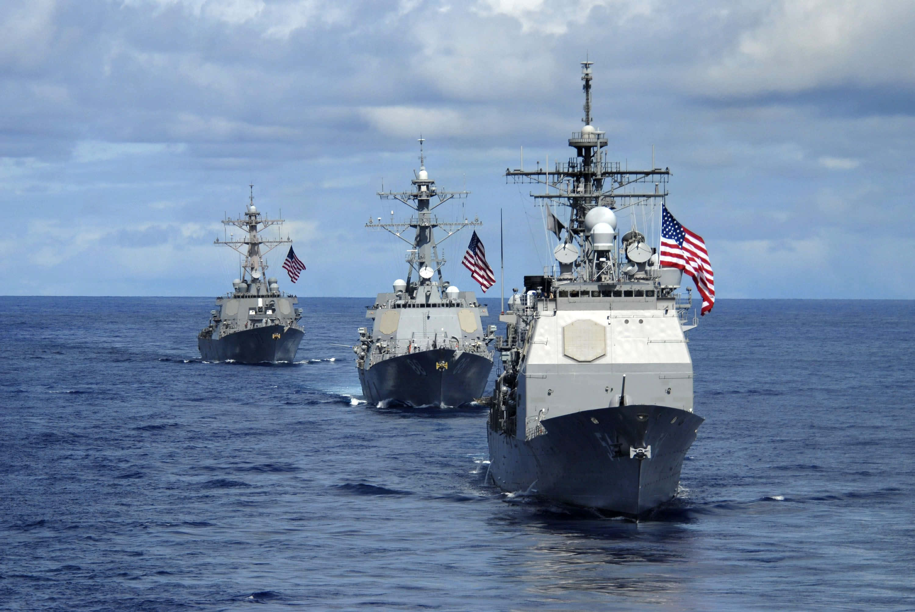 Navy 桌布 壁紙 — 三艘灰色的美國海軍軍艦在多雲的天空下，以編隊形式航行在廣闊的藍色海洋上。