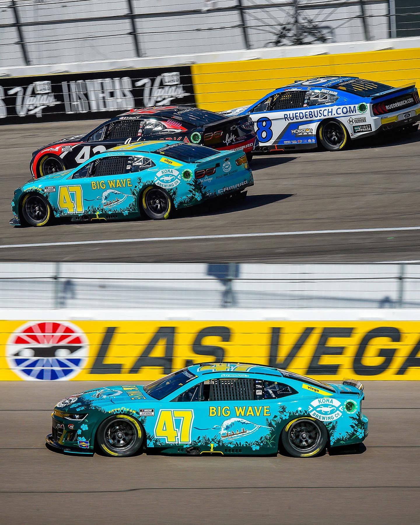 Racing 桌布 壁紙 — 三輛NASCAR賽車在拉斯維加斯賽道上疾馳，車身塗裝鮮豔，贊助商標誌在明亮的日光下清晰可見。