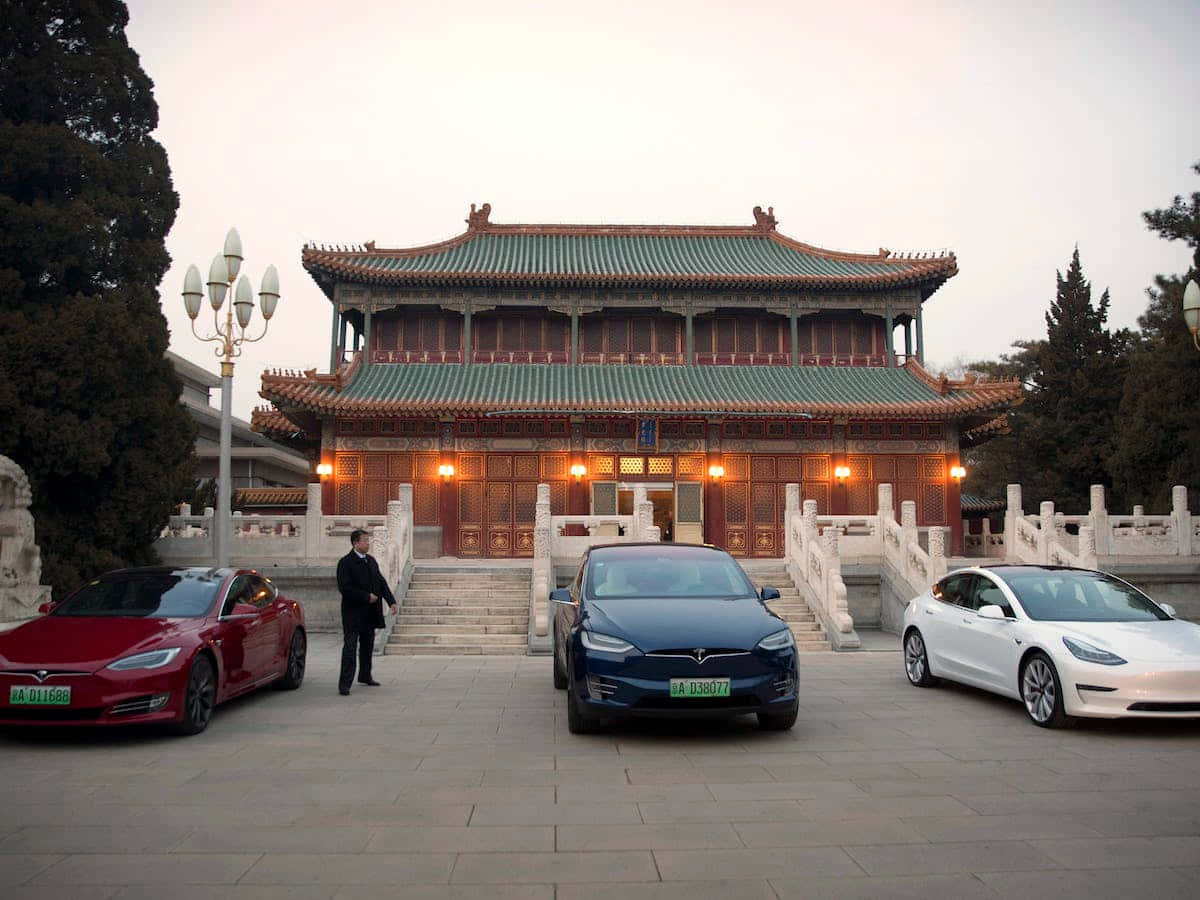 中國 桌布 壁紙 — 三輛Tesla汽車停在一座傳統中國寺廟前，溫暖的燈光在黃昏中閃爍。