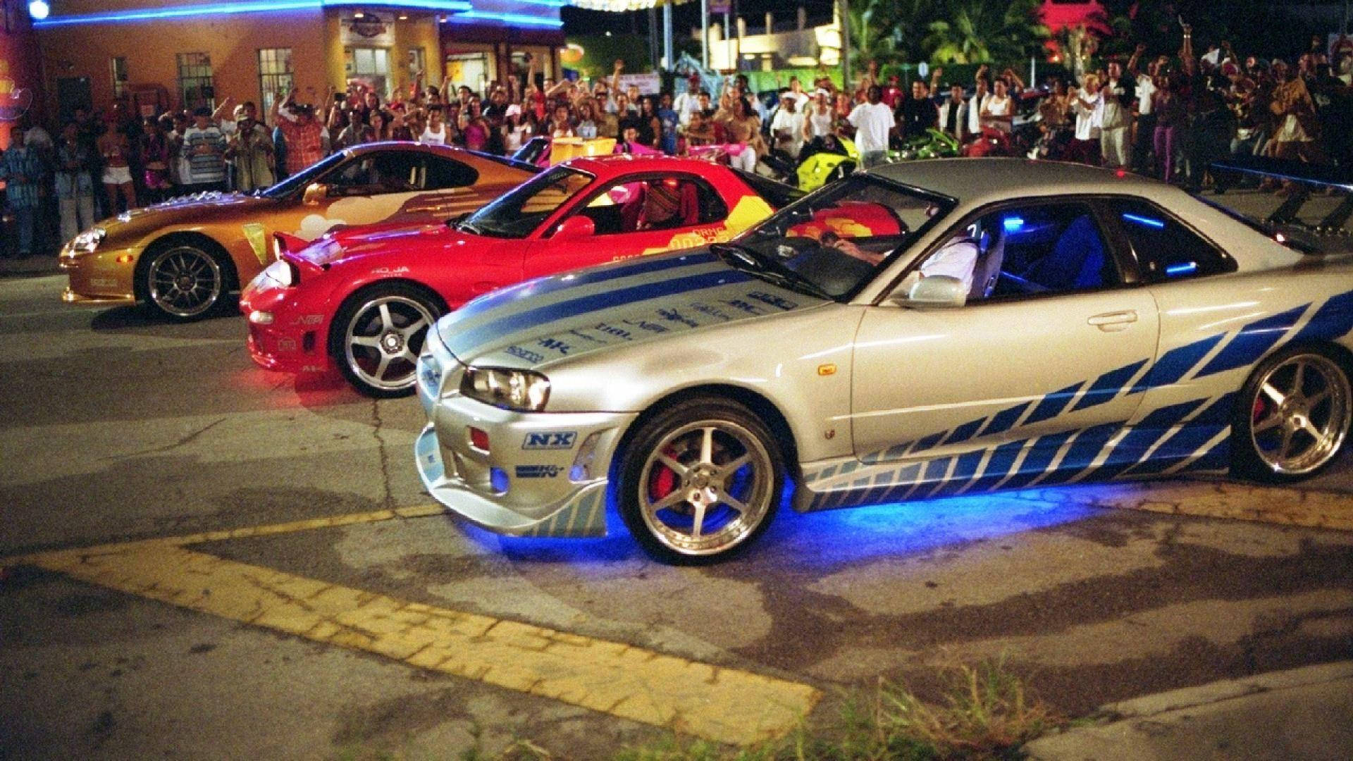 三輛定制跑車在夜間停泊，帶有發光的底盤燈，吸引圍觀人群。