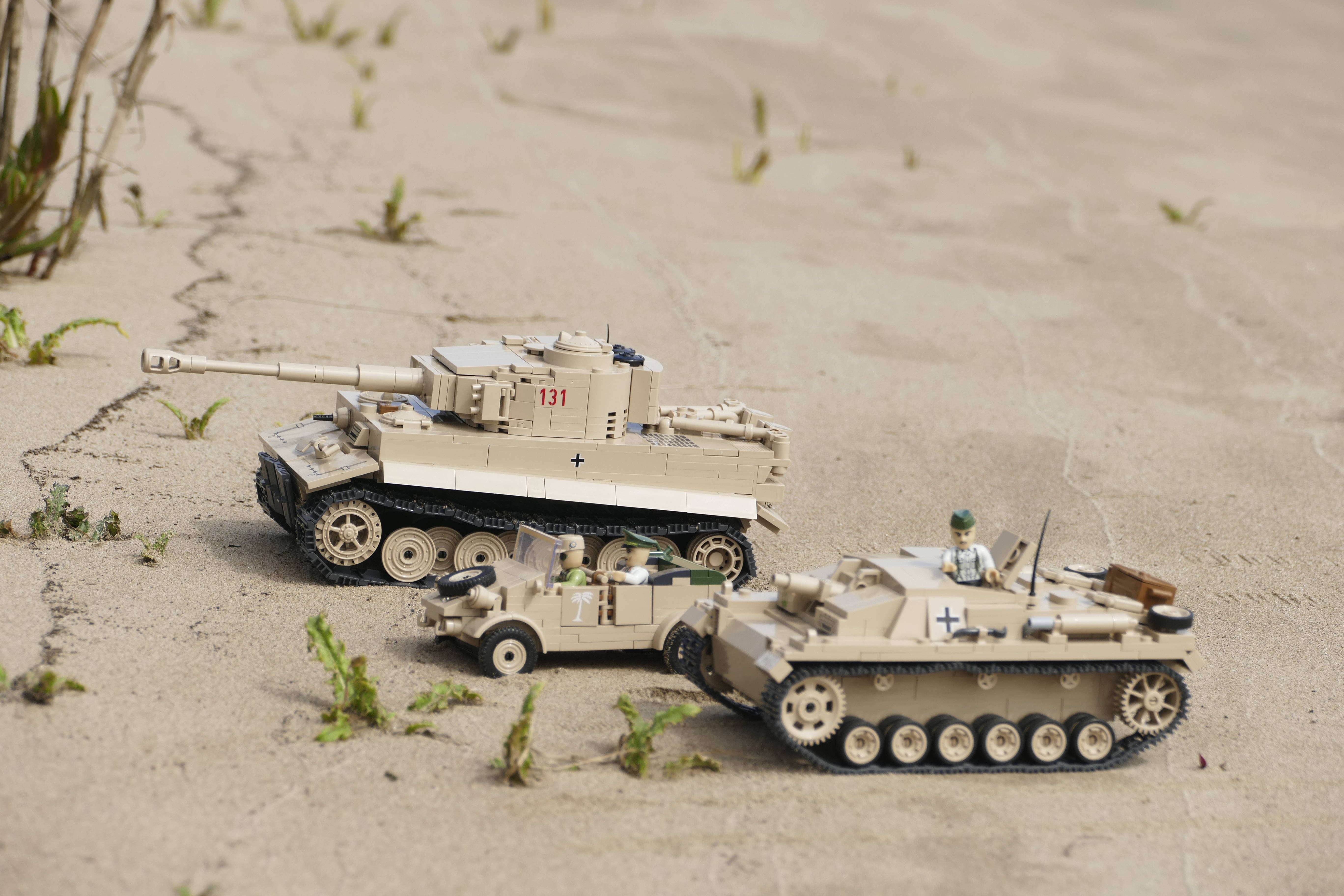 Tanks 桌布 壁紙 — 三輛帶有十字架和數字的米色軍事玩具車，放置在佈滿裂縫的沙地上，周圍有稀疏的綠色雜草。