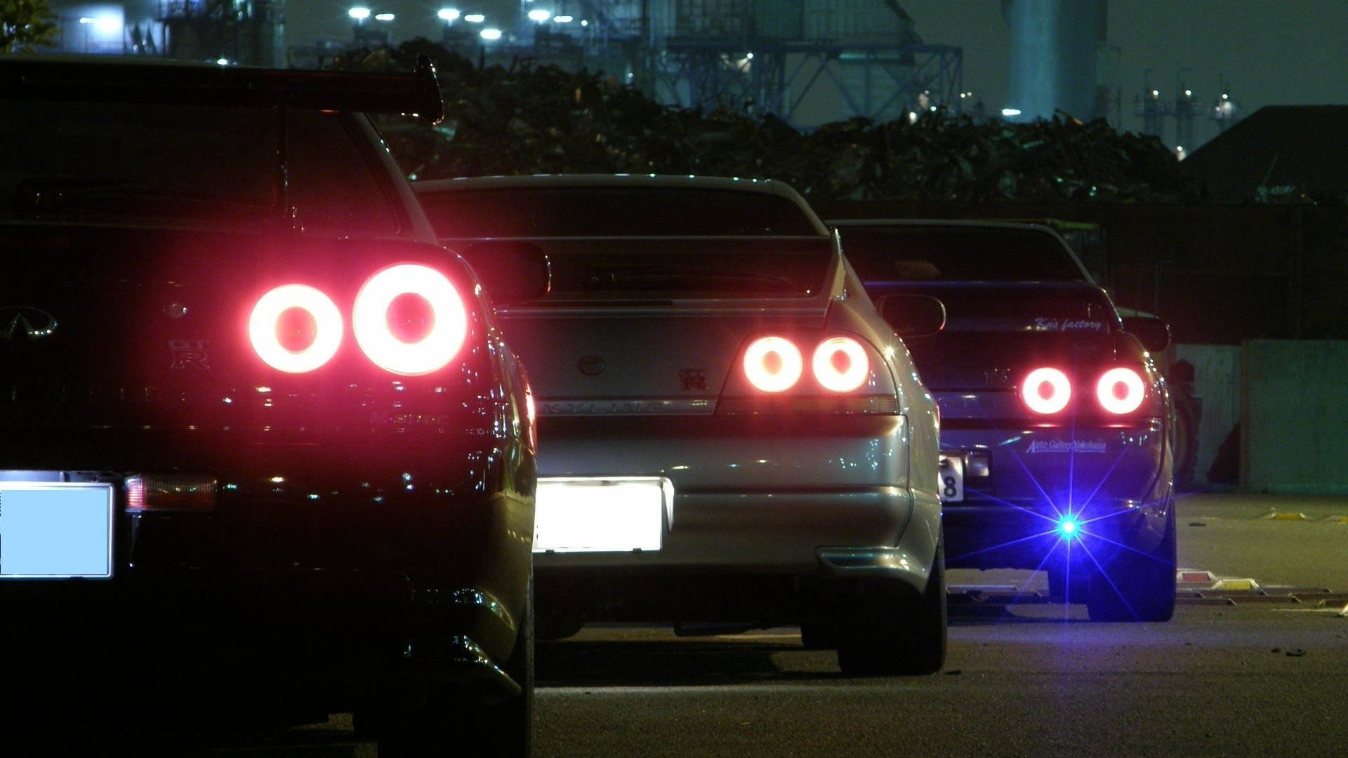JDM 桌布 壁紙 — 三輛帶有發光紅色圓形尾燈的跑車夜間停放在工業區。