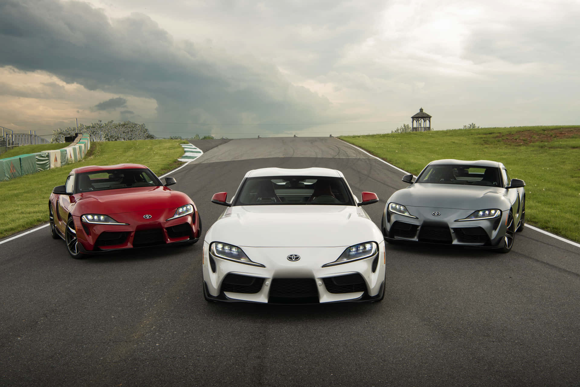 三輛豐田Supra跑車在暴風雲下的賽道上。 — Toyota Supra Mk4 壁紙