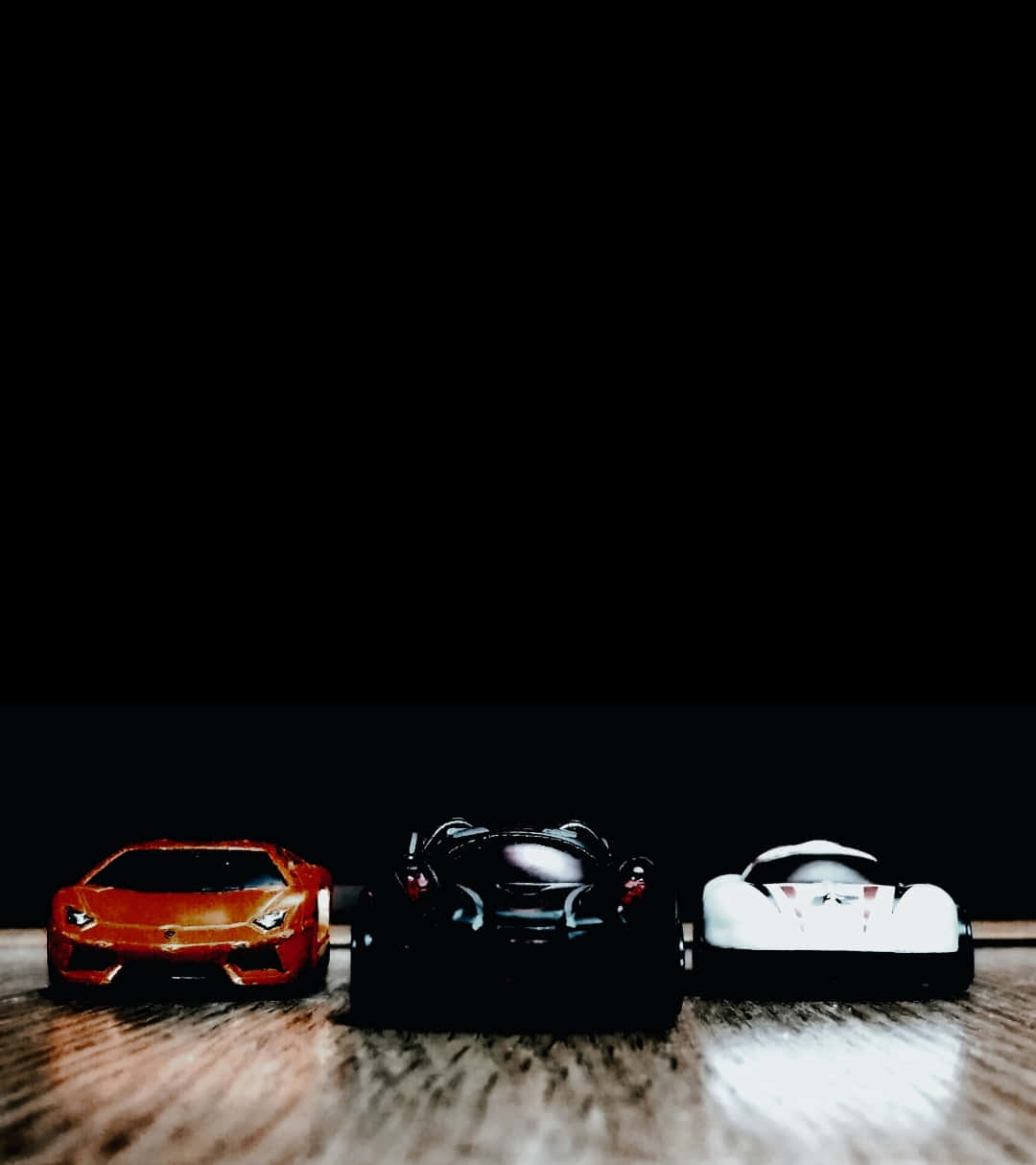 Sport Cars from front 壁紙 — 三輛玩具跑車紅色黑色和白色排成一排放在黑色背景的木地板上。