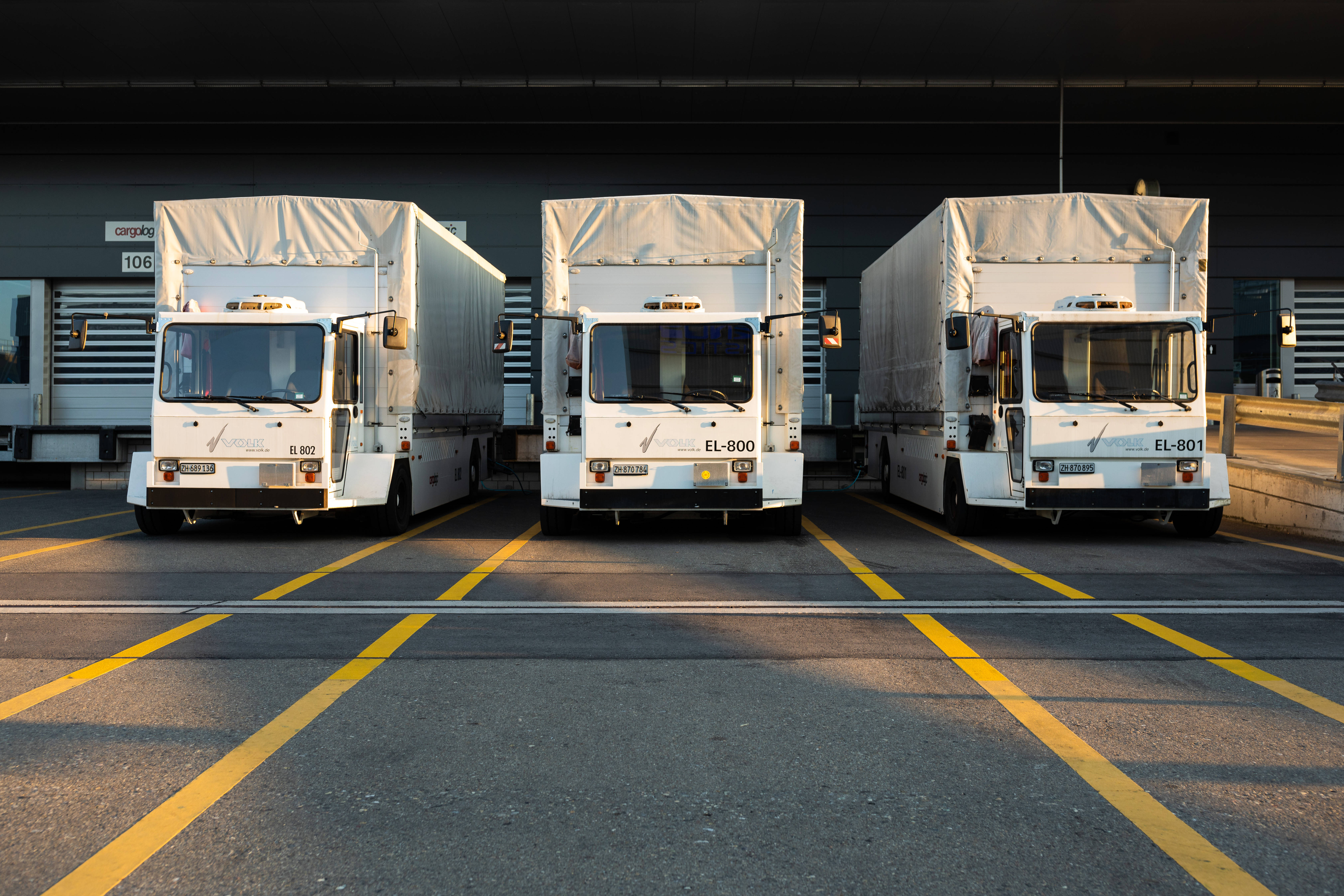 Truck 桌布 壁紙 — 三輛白色貨車在溫暖的黃金時段光線下排成一排停靠在裝卸碼頭。