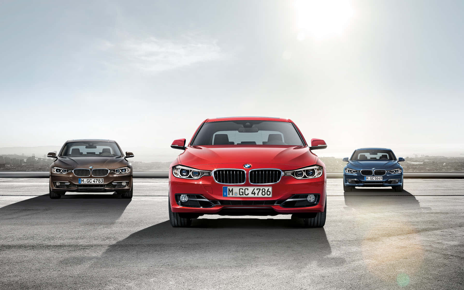 BMW 動圖 桌布 壁紙 — 三輛紅色、棕色和藍色的BMW轎車排成一排，站在陽光普照的屋頂上，俯瞰城市景觀。
