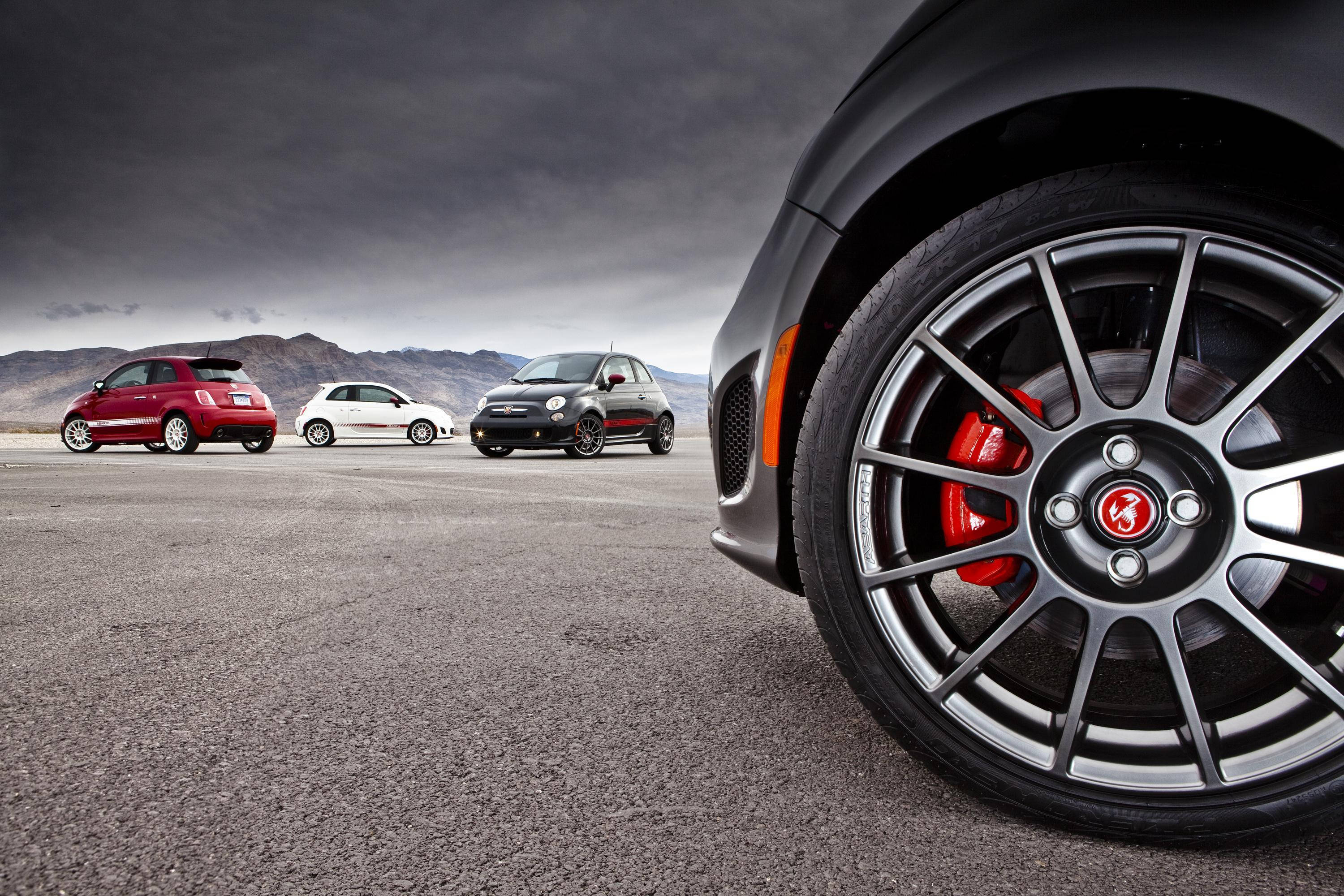 Fiat 桌布 壁紙 — 三輛紅色、白色和黑色的Fiat 500汽車站在沙漠公路上，天空風暴，特寫黑色汽車的車輪顯示紅色制動卡鉗。