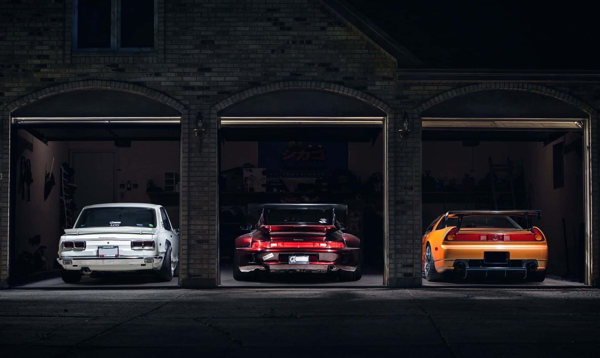 Garage 桌布 壁紙 — 三輛經典汽車在夜間排成一排停在磚砌車庫內，帶有戲劇性燈光。