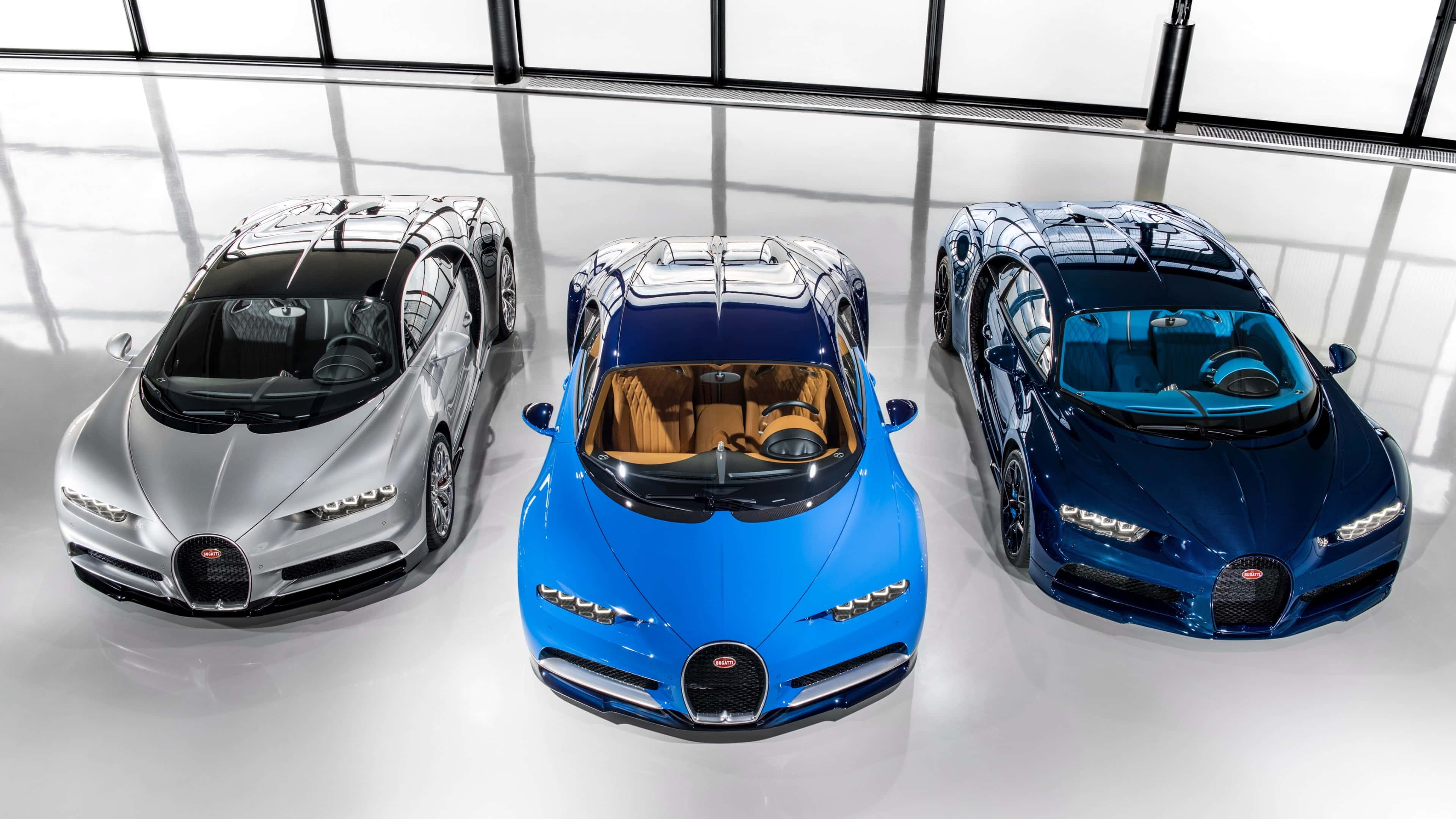 bugatti iPhone 桌布 壁紙 — 三輛銀藍色和深藍色的Bugatti超跑在明亮的攝影棚燈光下，在反光的白色地板上閃閃發光。