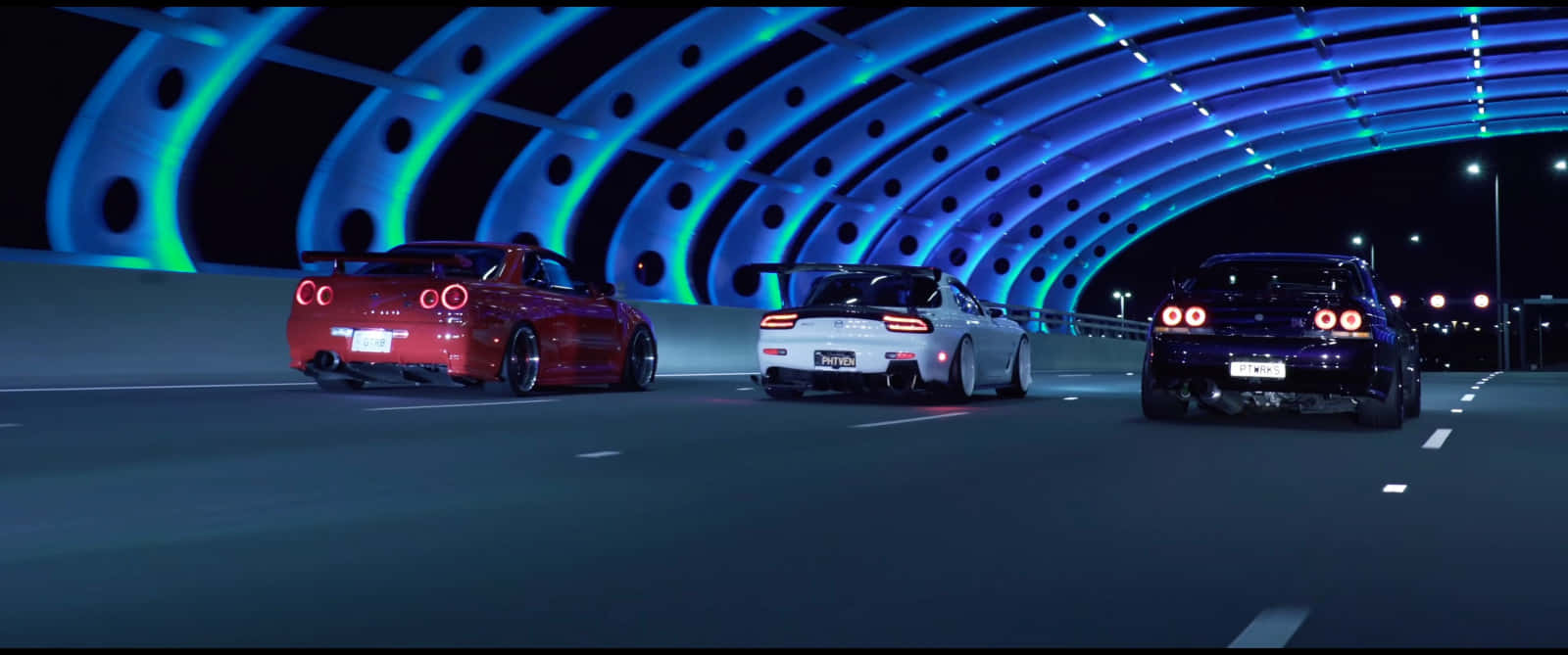 R33 GT-R 桌布 壁紙 — 三輛高性能跑車在夜間穿過發光的藍色隧道，伴隨著鮮豔的霓虹燈光。