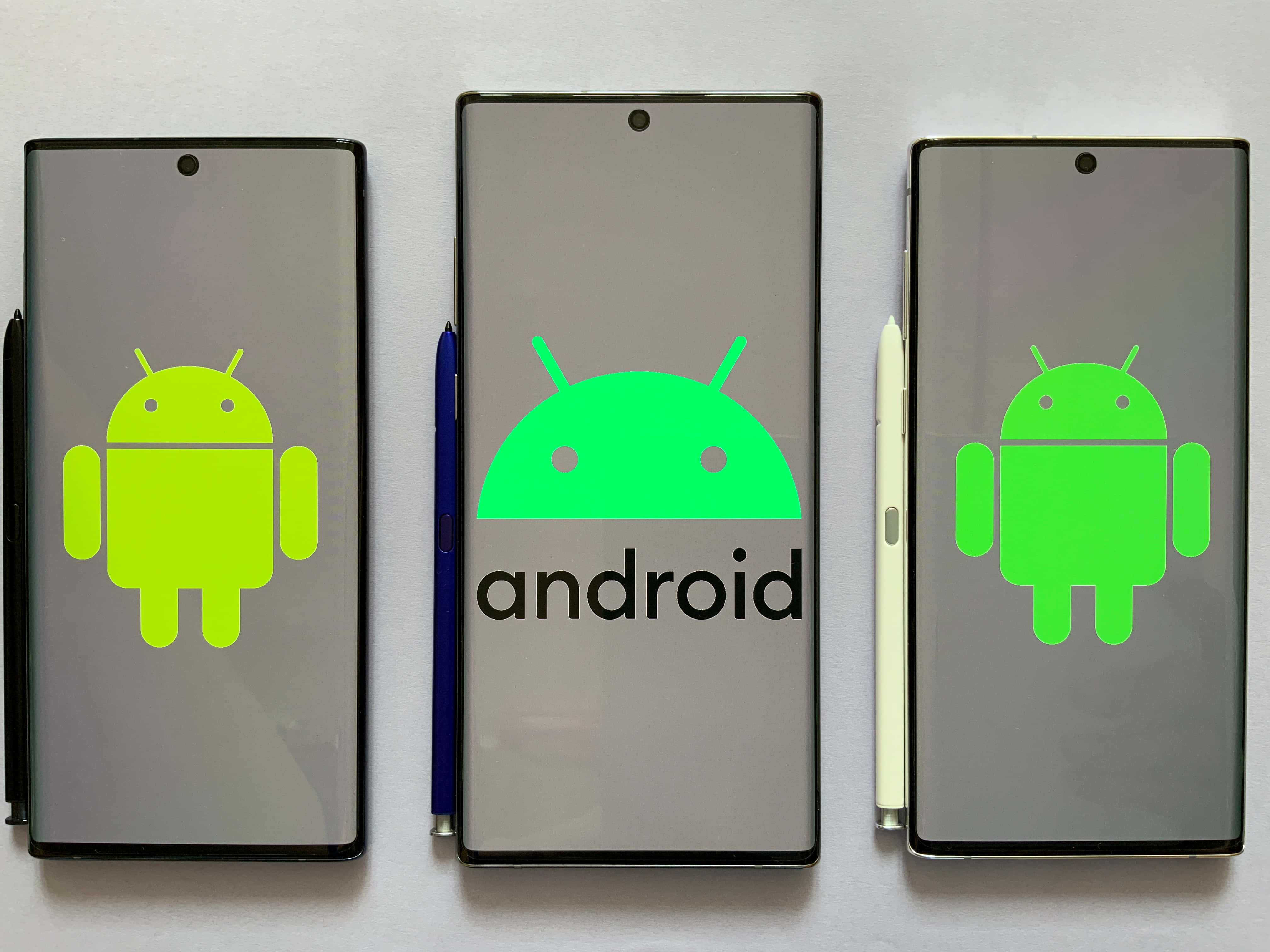 安卓 桌布 壁紙 — 三部 Android 智慧型手機在純白色背景上顯示綠色 Android 標誌和文字商標。