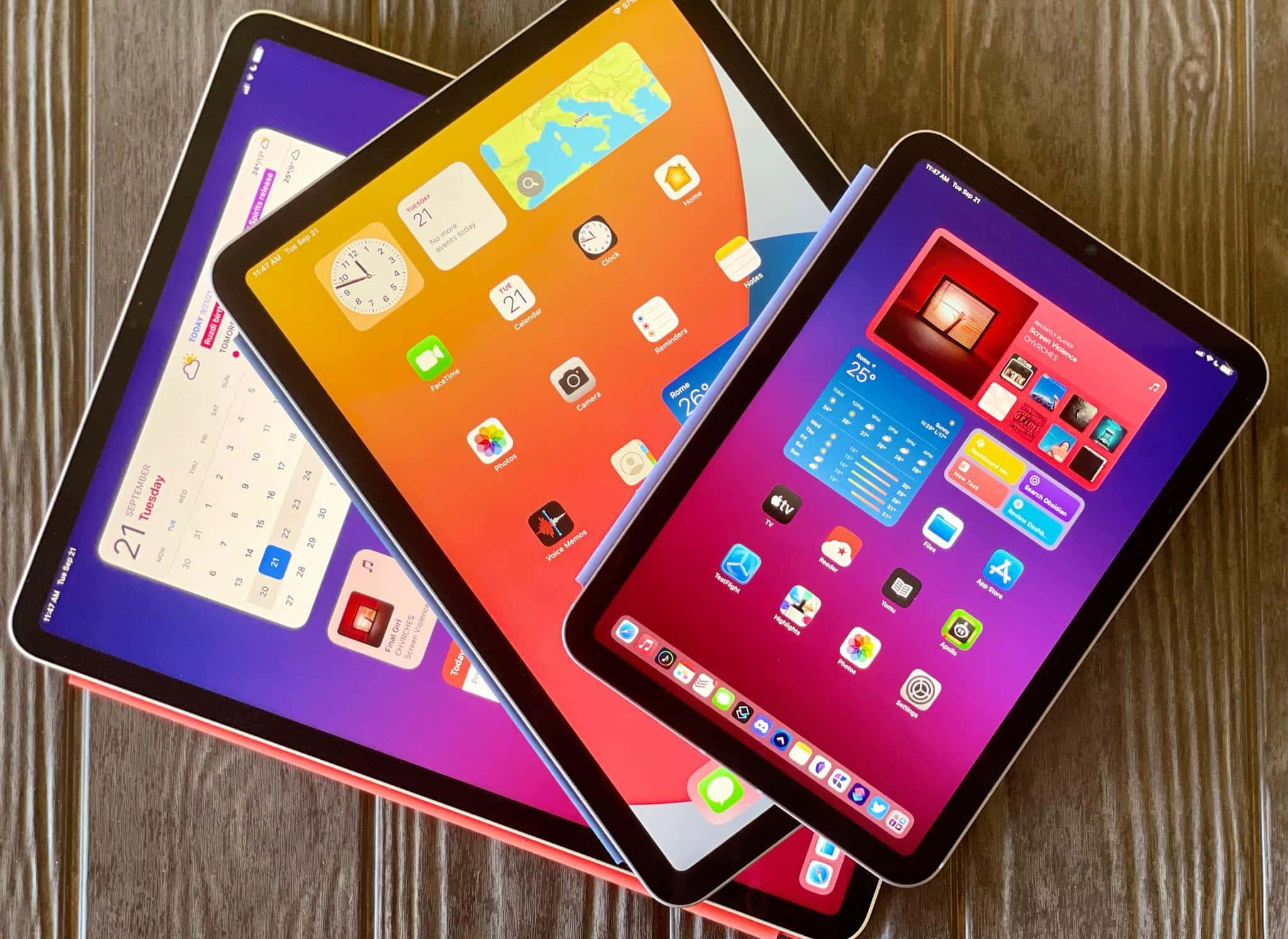iPad 桌布 壁紙 — 三部色彩繽紛的平板電腦顯示充滿活力的主螢幕，堆疊在木質表面上。