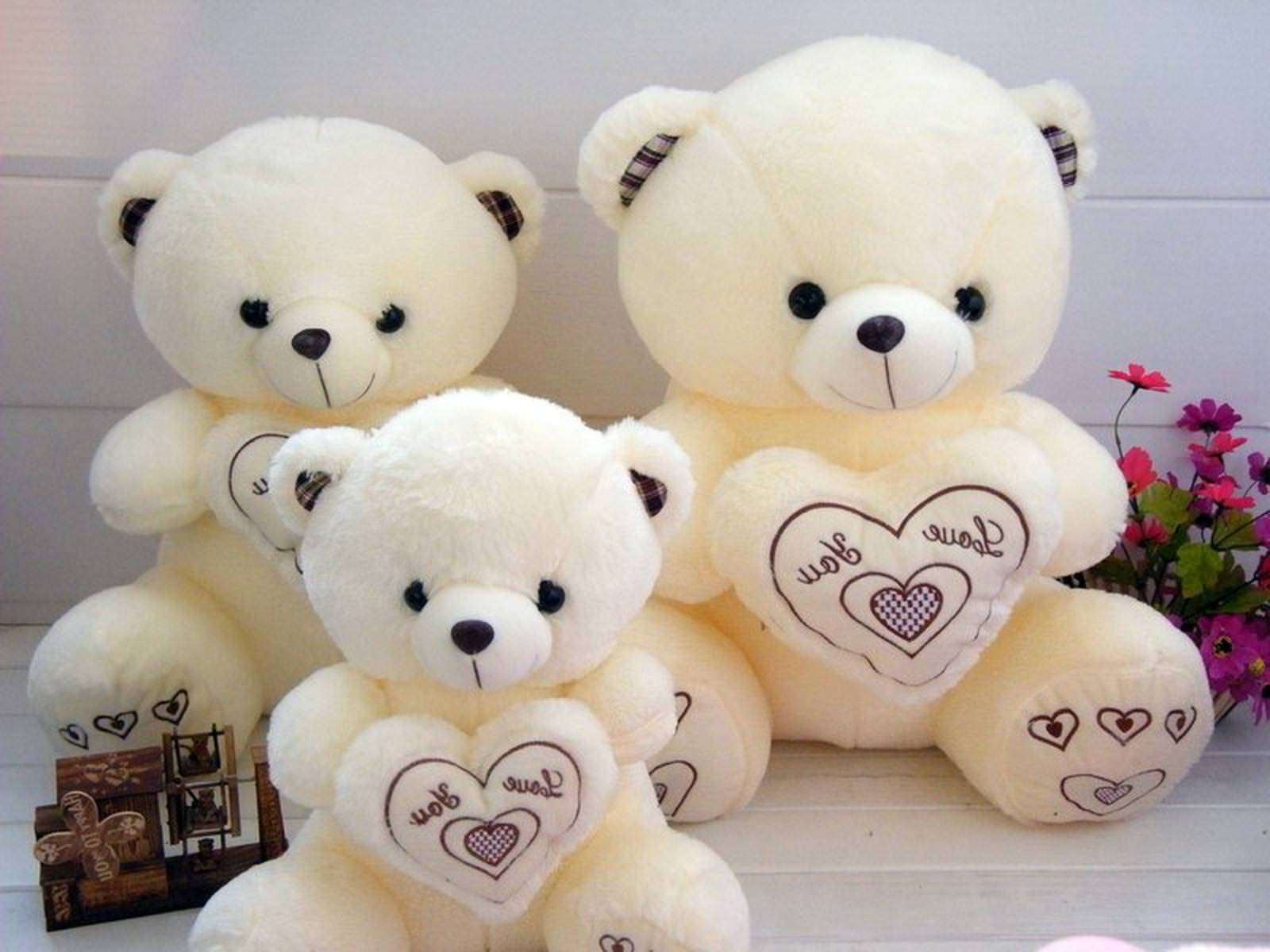 Cute Bear 桌布 壁紙 — 三隻不同大小的奶油色泰迪熊坐在一起，手持寫有「Love You」的心形，旁邊有一束粉紅色花朵。