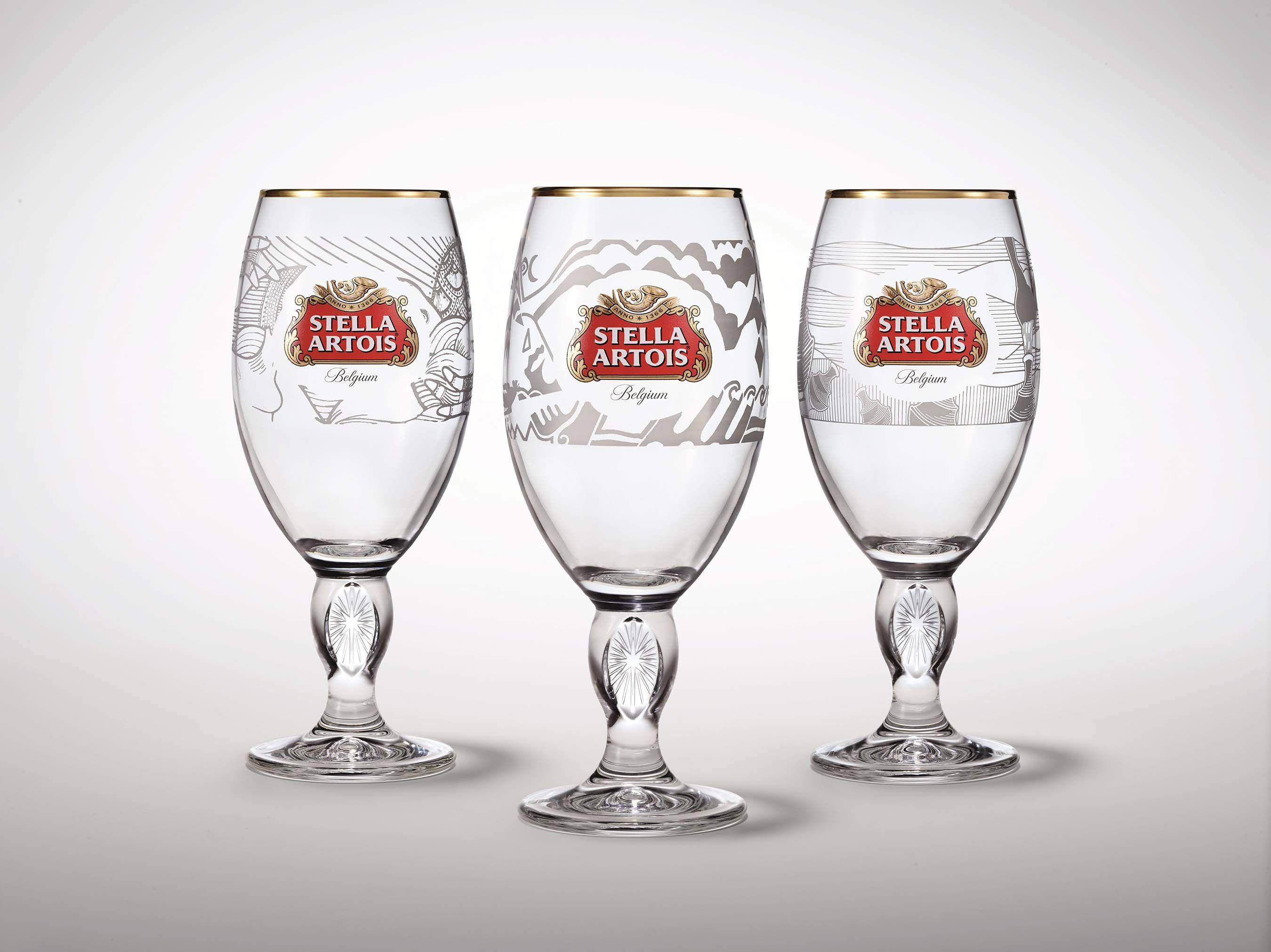 飲料 桌布 壁紙 — 三隻優雅的 Stella Artois 啤酒杯，帶有金色邊緣和精緻蝕刻圖案，排列在柔和的漸變背景前。