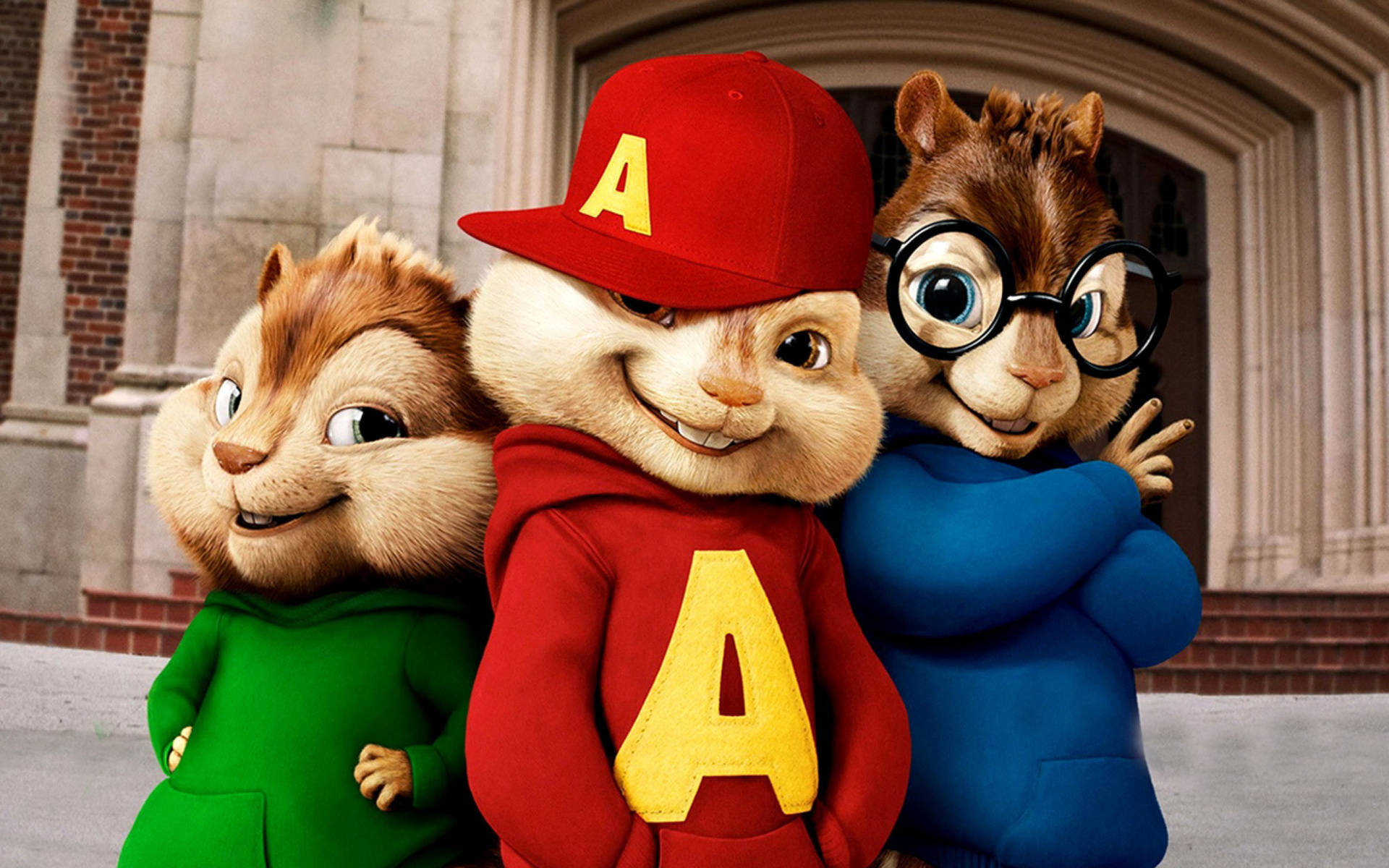 Chipmunks 桌布 壁紙 — 三隻動畫花栗鼠穿著彩色連帽衫和紅色帽子，在石頭建築入口前愉快地擺姿勢。