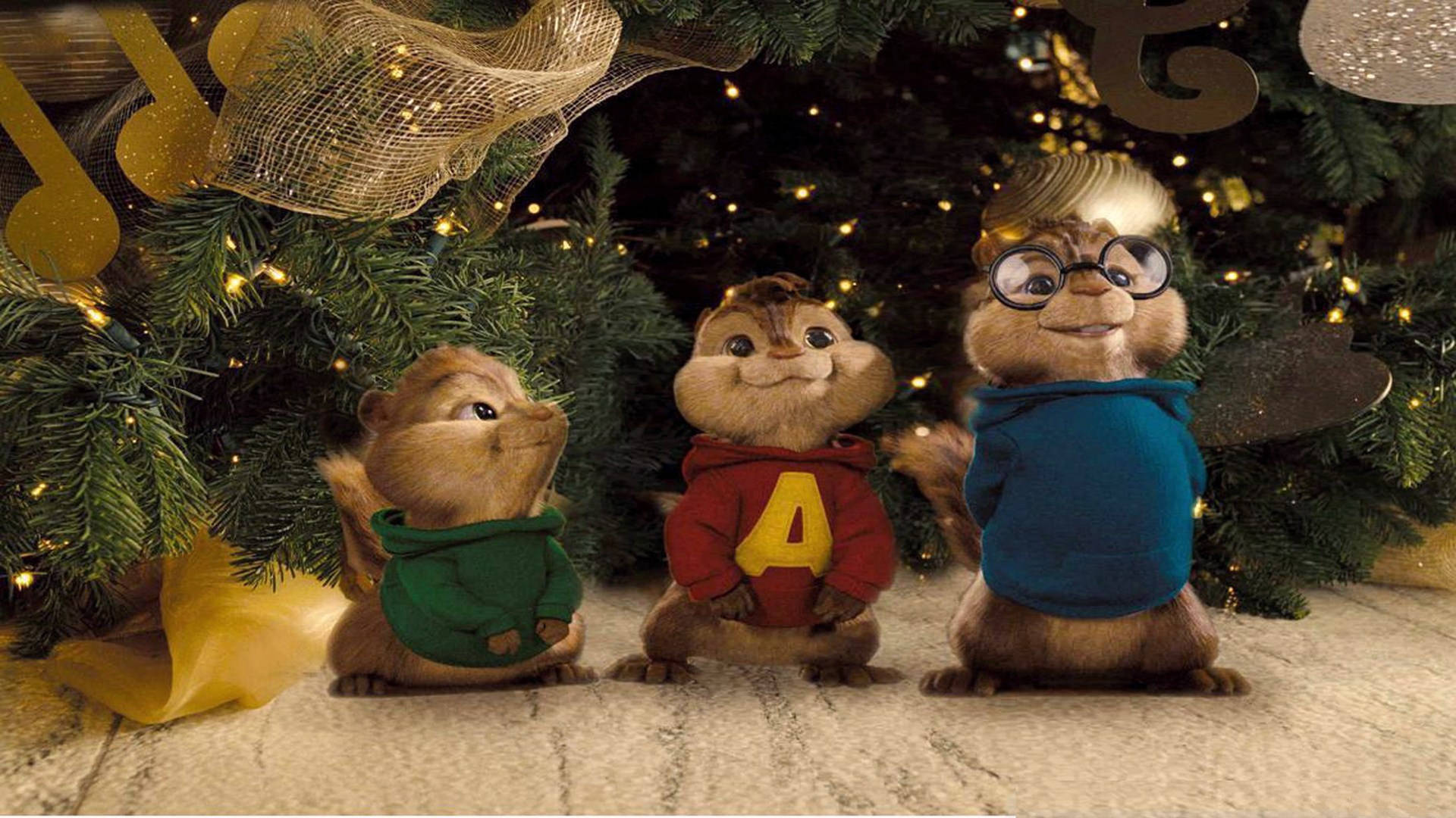 Chipmunks 桌布 壁紙 — 三隻動畫花栗鼠穿著毛衣坐在裝飾著閃爍燈光和金色飾品的聖誕樹下。