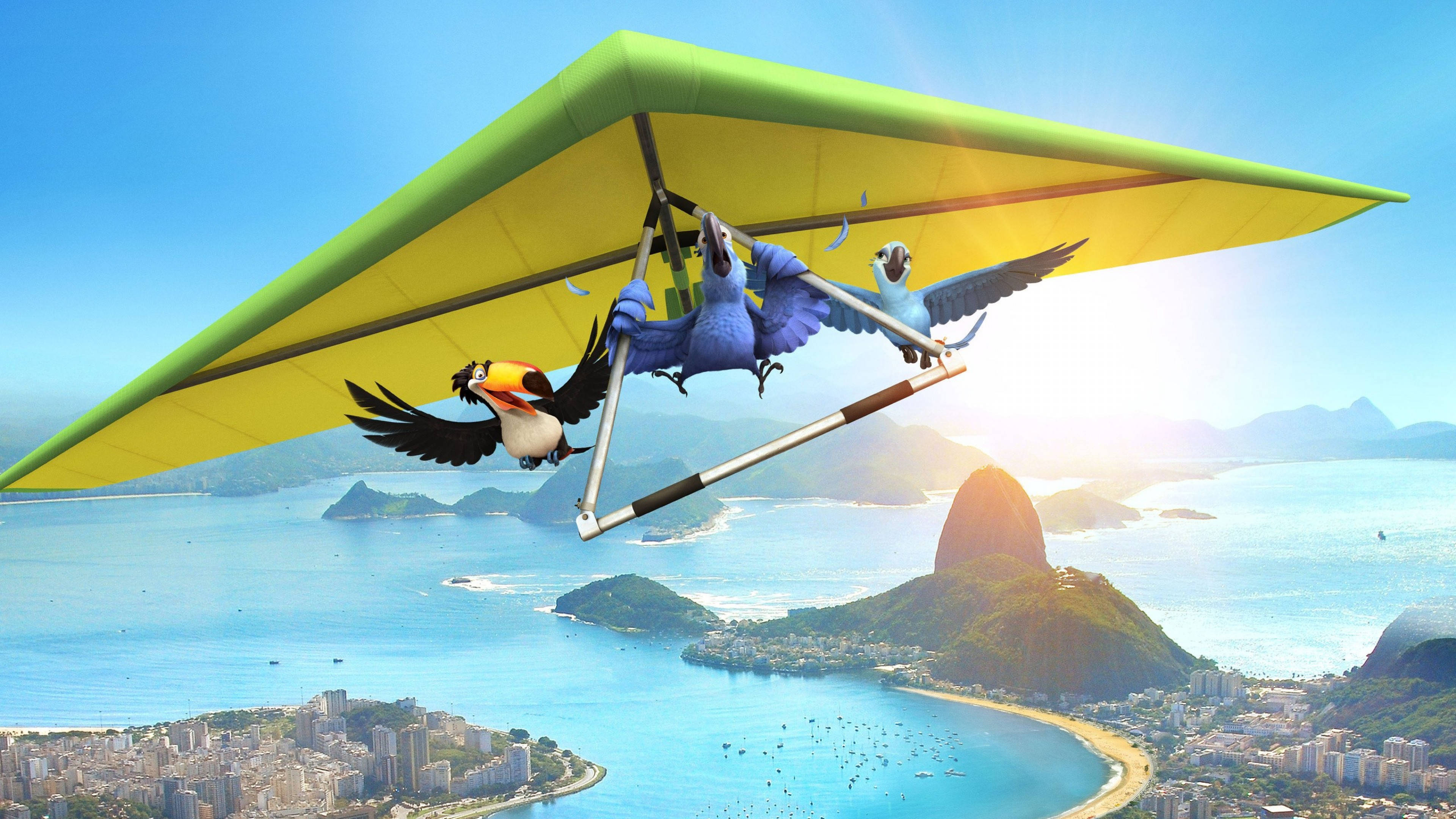 rio 桌布 壁紙 — 三隻動畫鳥在黃色滑翔翼上翱翔於里約熱內盧標誌性的甜麵包山和閃閃發光的海灣之上。