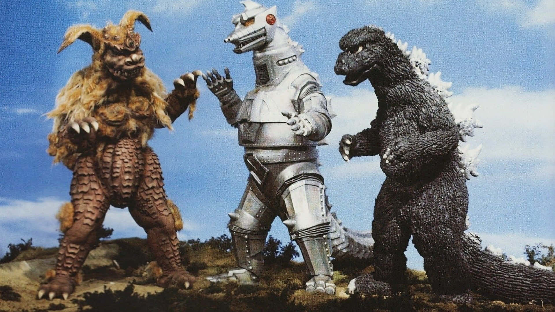 Godzilla Vs Mechagodzilla 桌布 壁紙 — 三隻巨型怪獸站在岩石山上，天空湛藍，雲朵零星分佈。