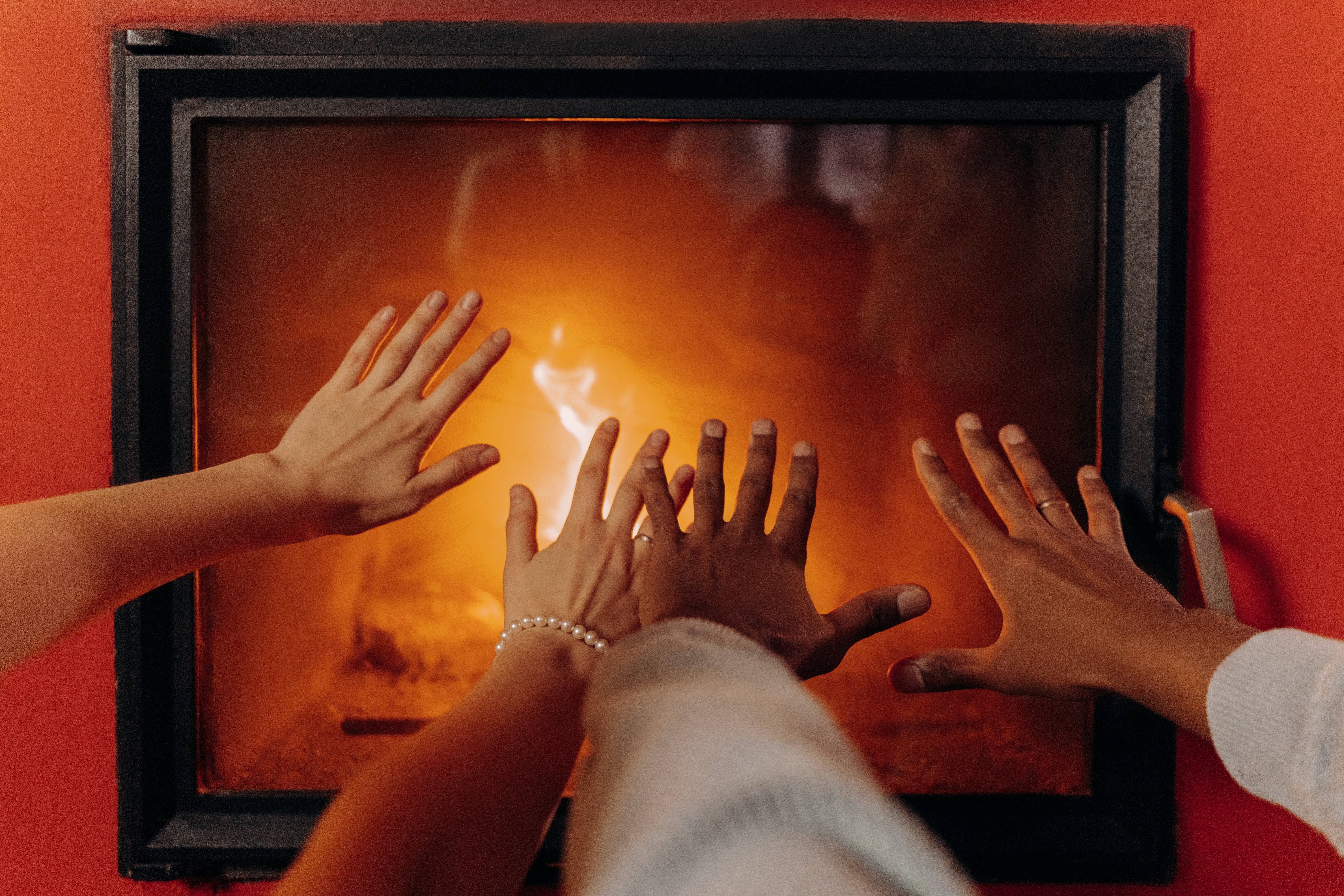 Couple Hands 桌布 壁紙 — 三隻手伸向一個在鮮紅色牆壁中發光的壁爐，散發出溫暖和親密感。