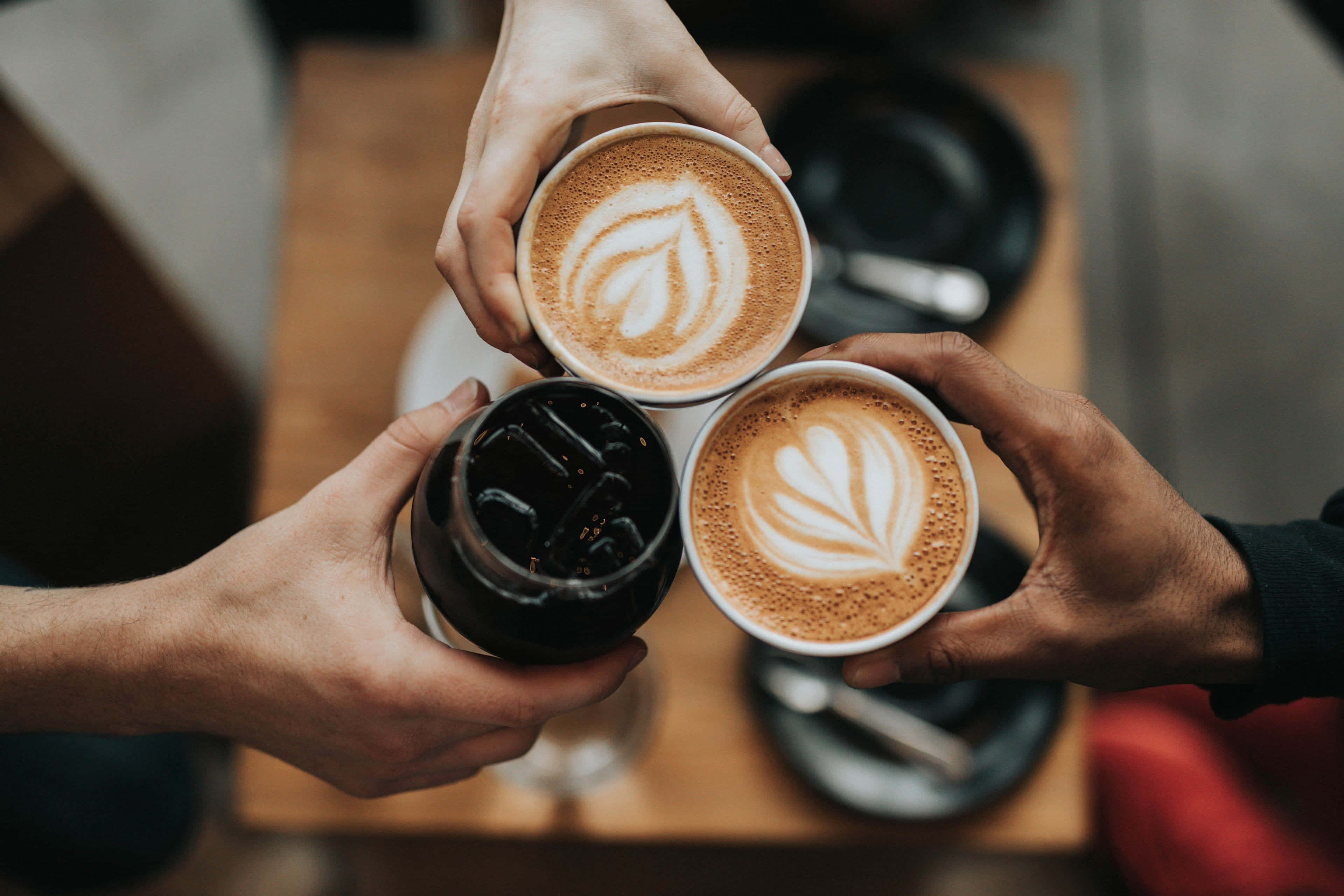 Iced Coffee 桌布 壁紙 — 三隻手在木桌上碰杯咖啡飲品慶祝。