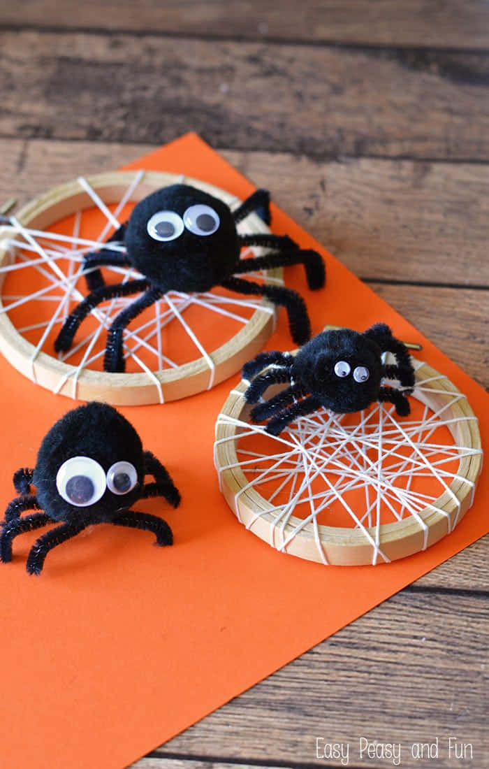 Spider 桌布 壁紙 — 三隻手工製作的黑色絨球蜘蛛，帶有凸眼，坐在木質表面上橙色紙張上的白色繩網上。