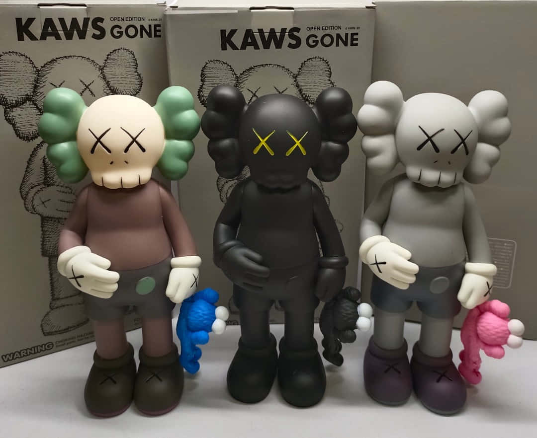 KAWS 桌布 壁紙 — 三隻米色、黑色和灰色的KAWS「Gone」搪膠公仔並排站立，手持毛絨玩具靠著其品牌盒子。