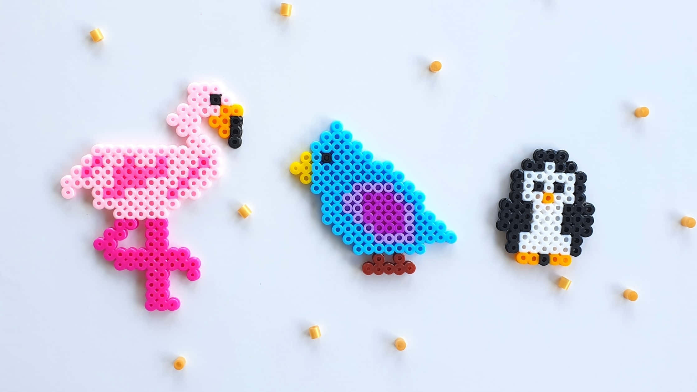 Bead 桌布 壁紙 — 三隻色彩繽紛的拼豆鳥：粉紅火烈鳥、藍鳥和黑色企鵝，站在白色表面上，周圍散落著珠子。