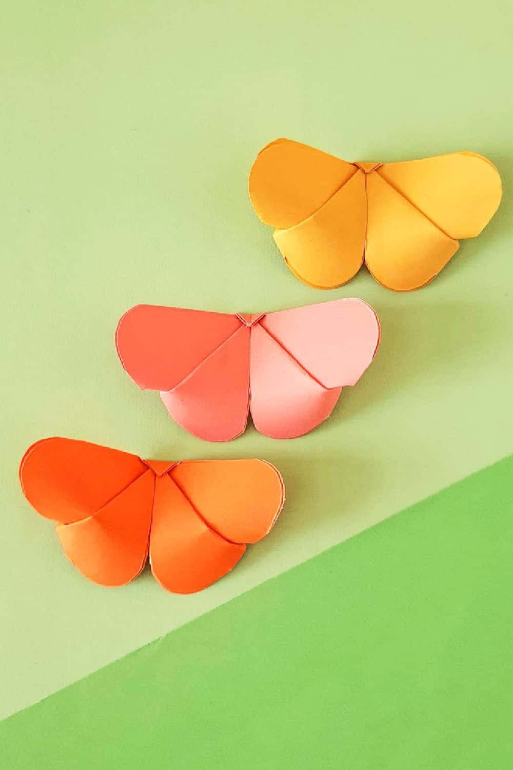 Butterfly Origami 桌布 壁紙 — 三隻色彩繽紛的摺紙蝴蝶，橙色、粉紅色和黃色，停留在一個分割的綠色背景上。