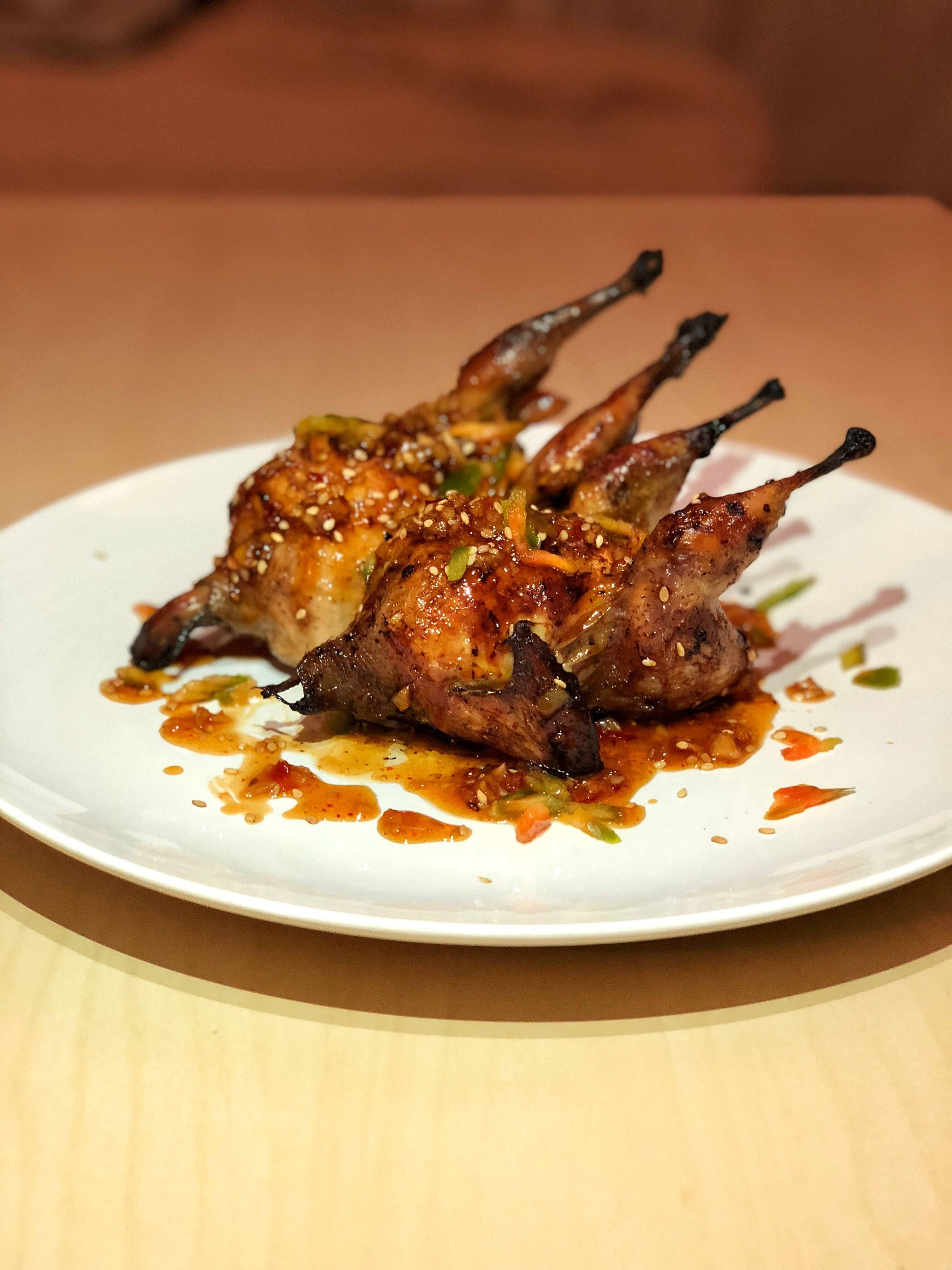 meat 桌布 壁紙 — 三隻釉面鵪鶉配芝麻和醬汁，優雅地擺放在白色盤子上。